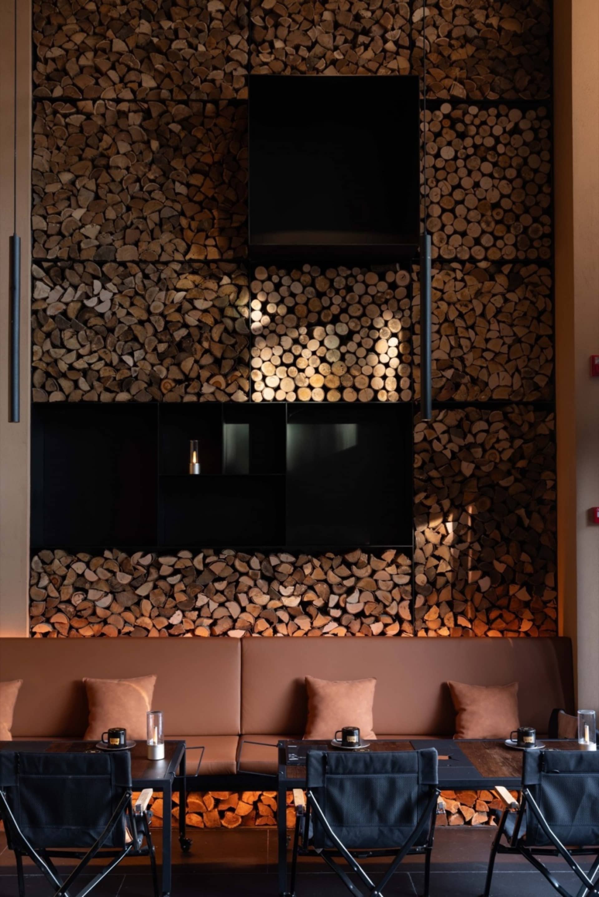 Cozy living space with a large wooden wall, two couches, three chairs, and two dining tables, with various decorative items scattered throughout