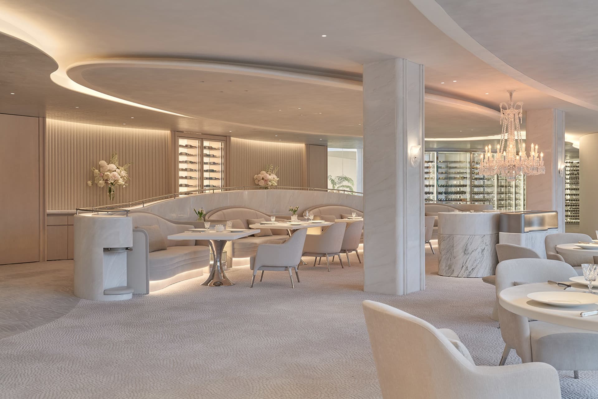 A large dining area with multiple tables and chairs, potted plants, and marble flooring, creating a sophisticated ambiance