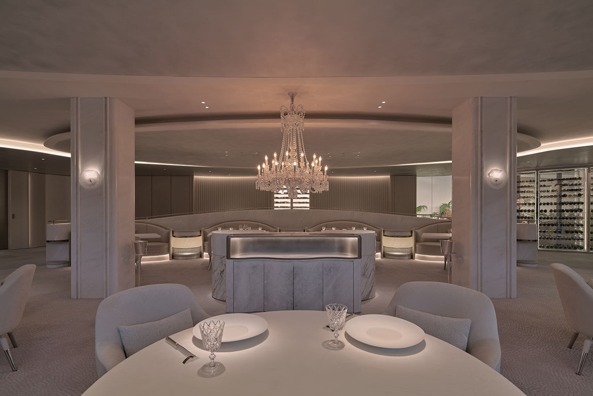 A formal dining space with a long table, chairs, and marble surfaces, set with plates and wine glasses, in a well-lit room with high ceilings and tasteful decorations