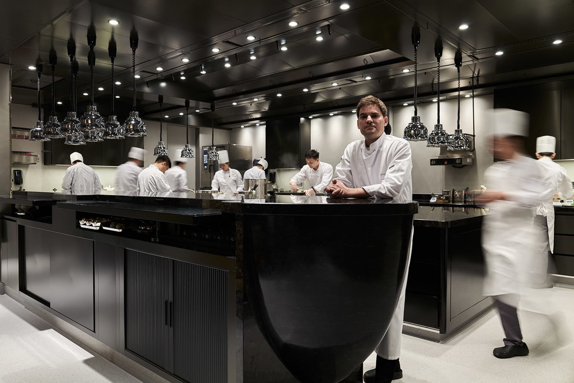 A bustling commercial kitchen with a black countertop island, multiple appliances, and several people working together