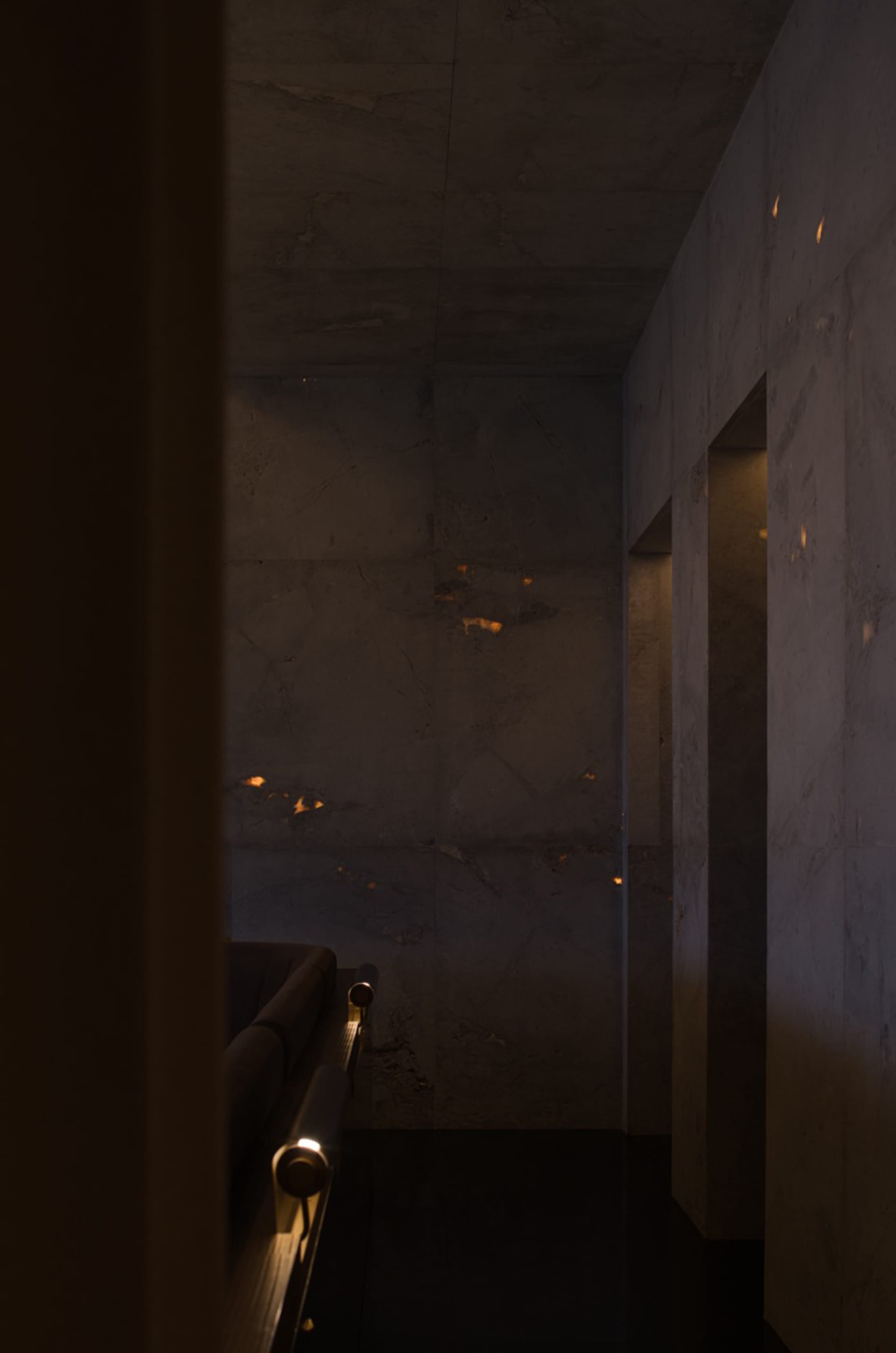 Dark living room with a couch in the corner, two benches, and dim lighting, featuring concrete walls