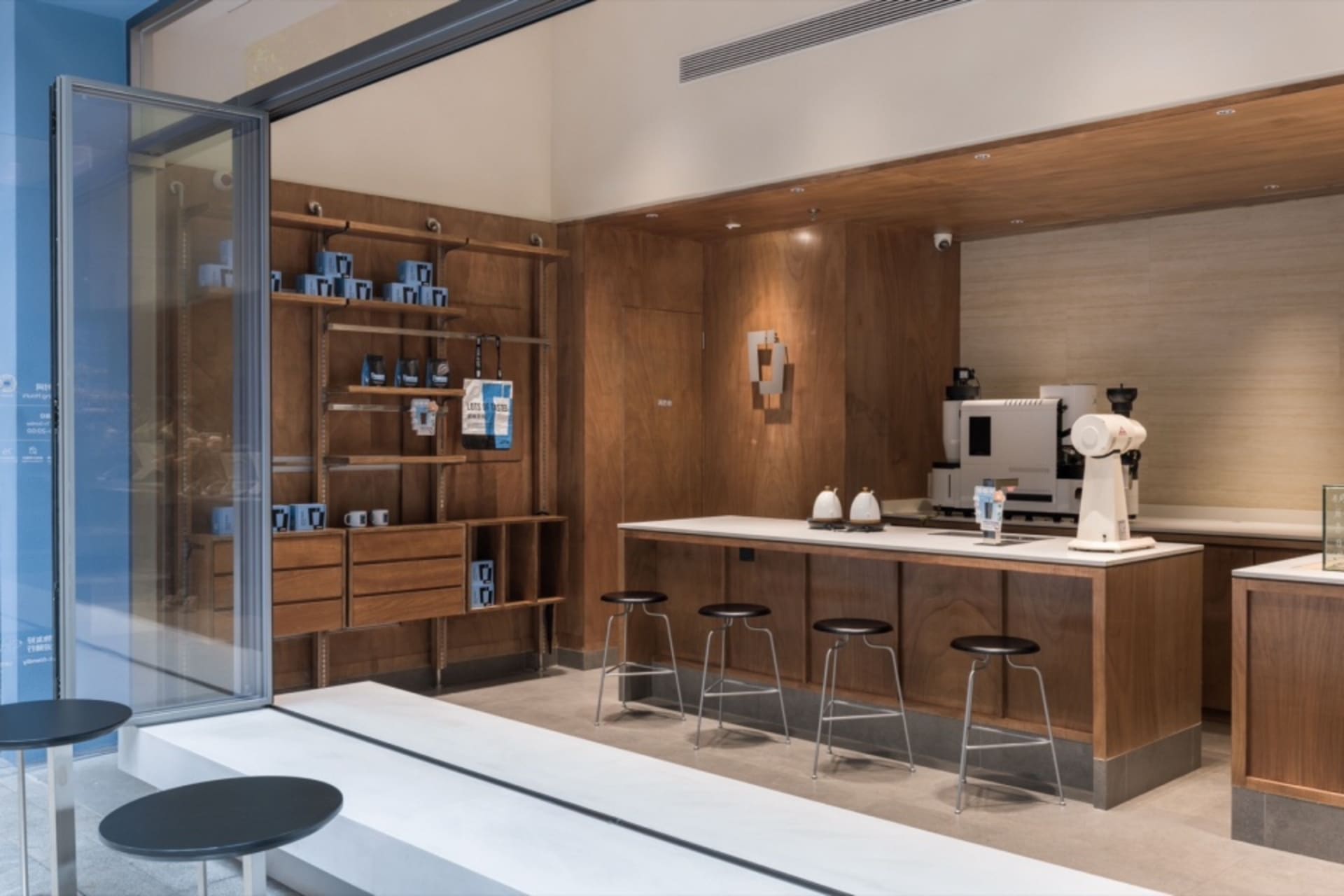A modern coffee shop display space with a counter, stools, and various coffee shop items on display
