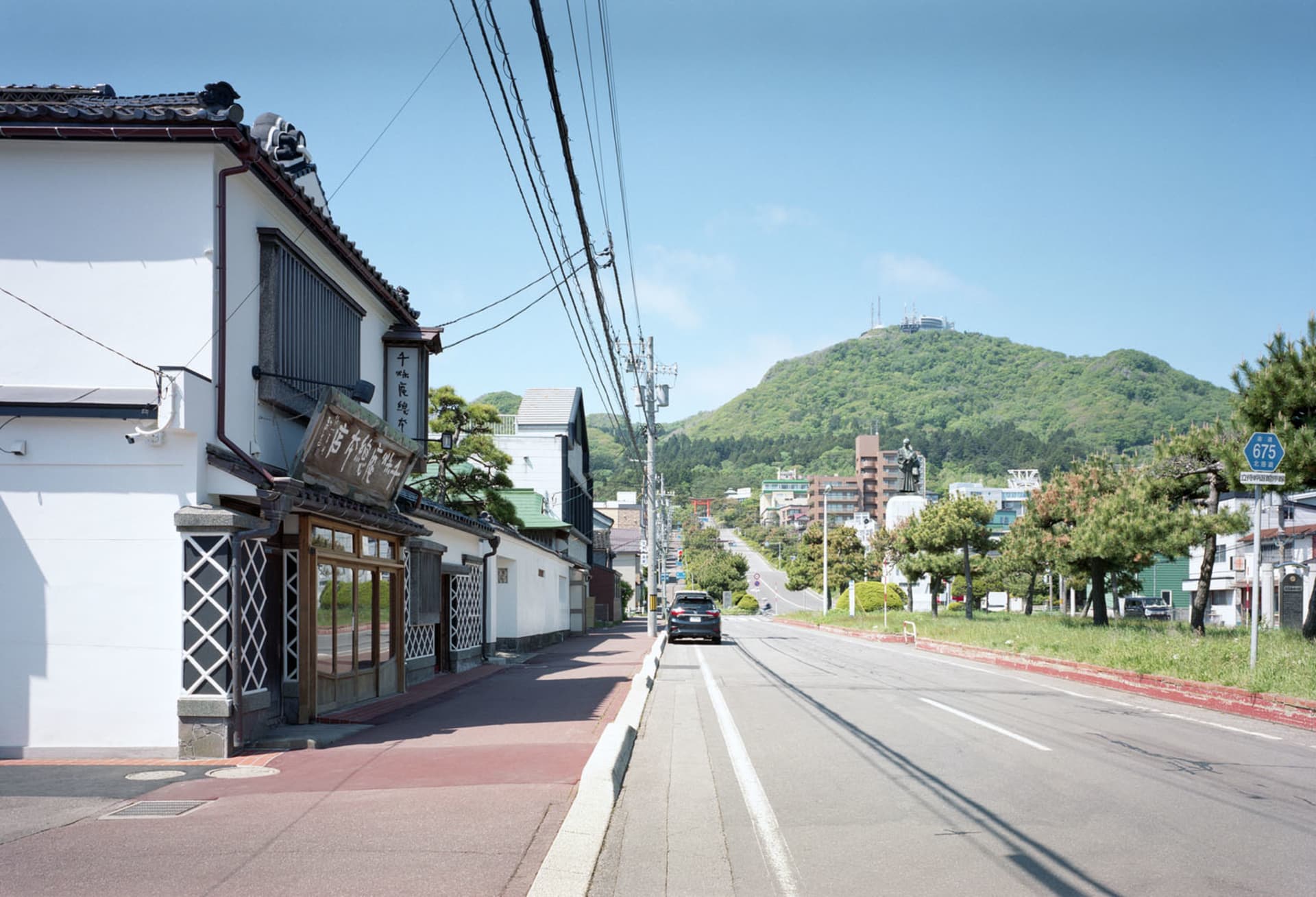 熱鬧的亞洲街景，白色建築頂著紅瓦屋頂，周圍有行人和停放的車輛，位於都市環境中