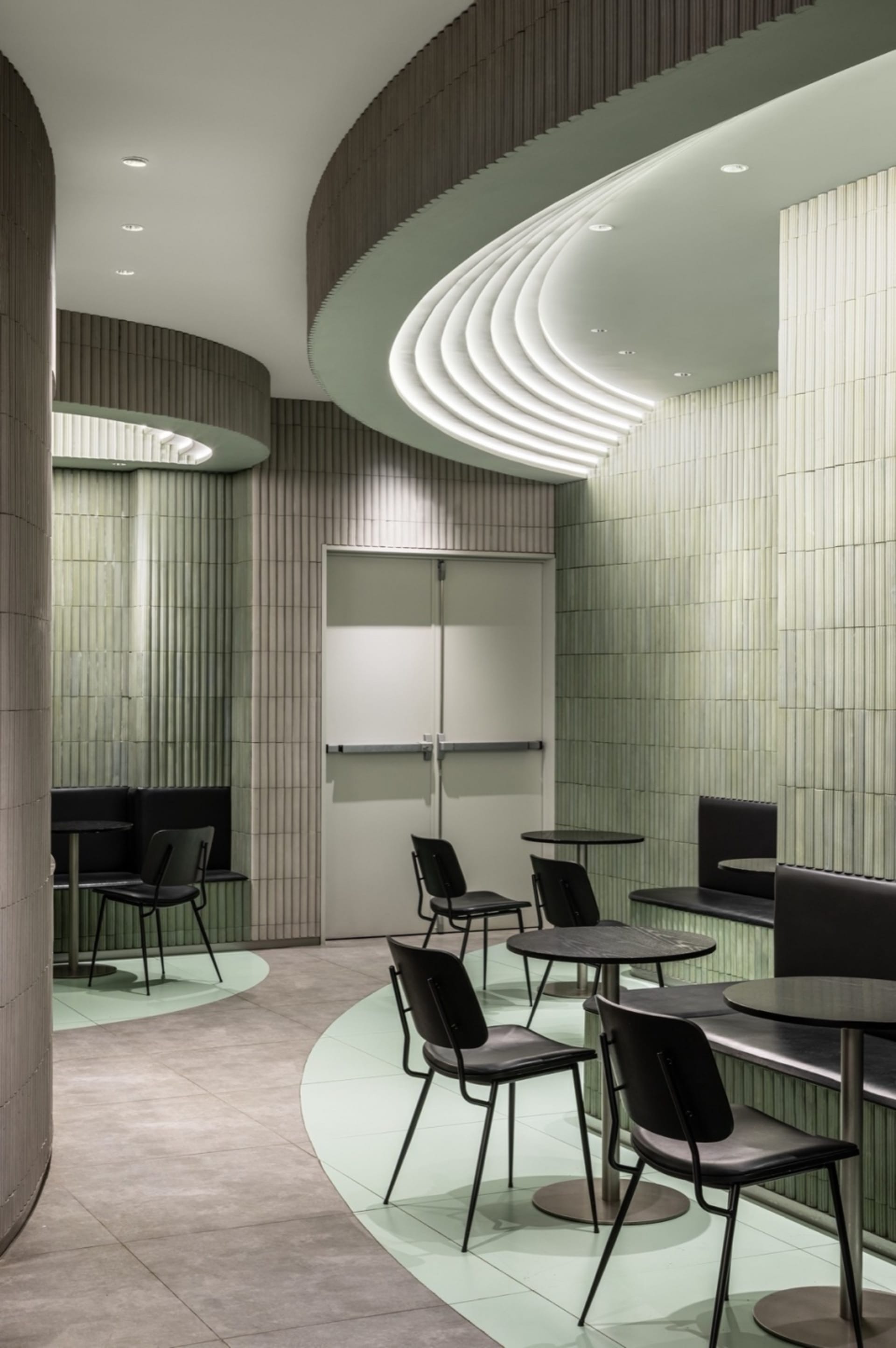 A restaurant interior with multiple tables and chairs, green tile walls, and a welcoming atmosphere