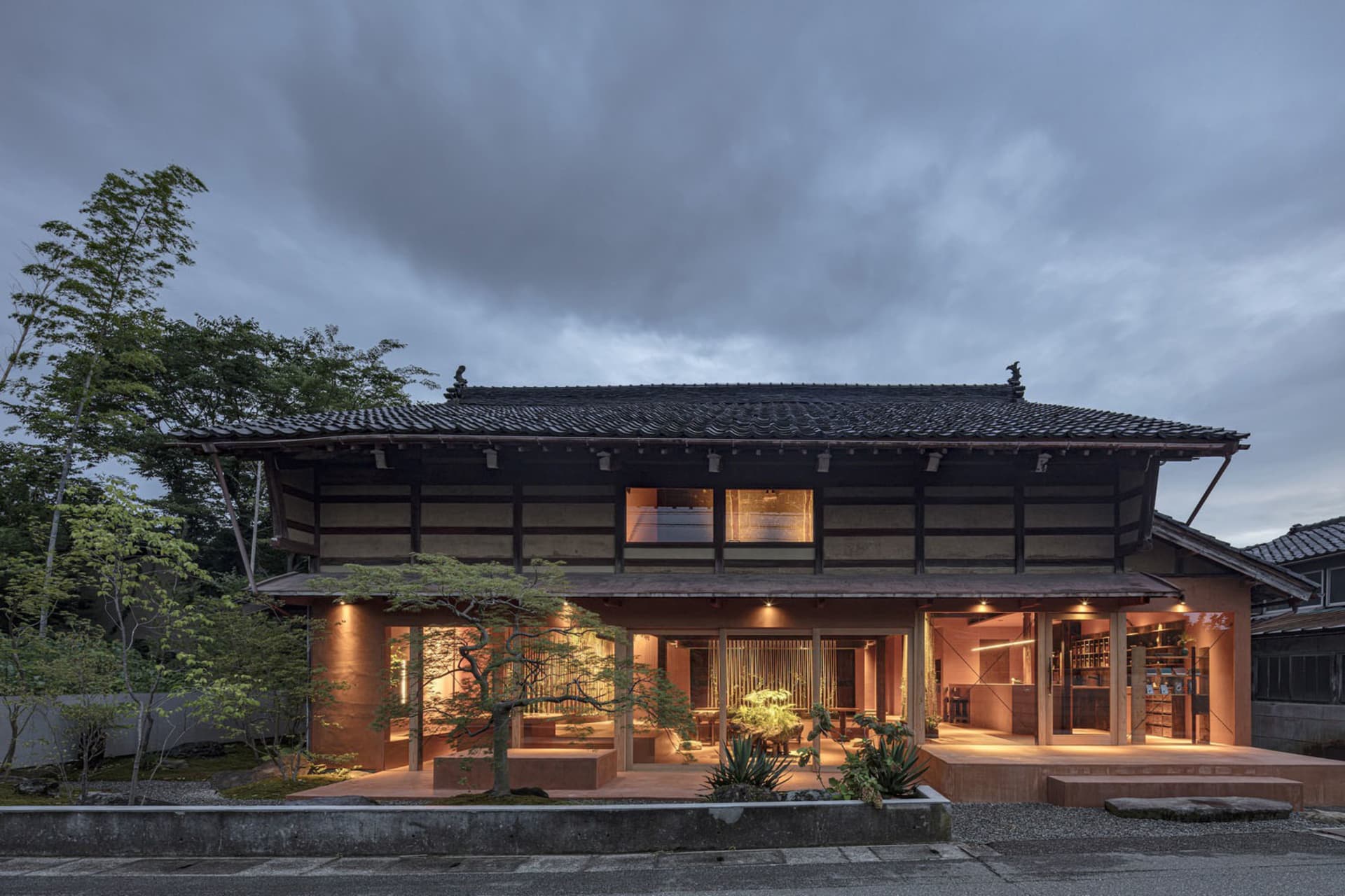 A traditional Asian-style house with a large wooden structure, tiled roof, and multiple windows, surrounded by potted plants and outdoor furniture, exuding a warm and inviting atmosphere