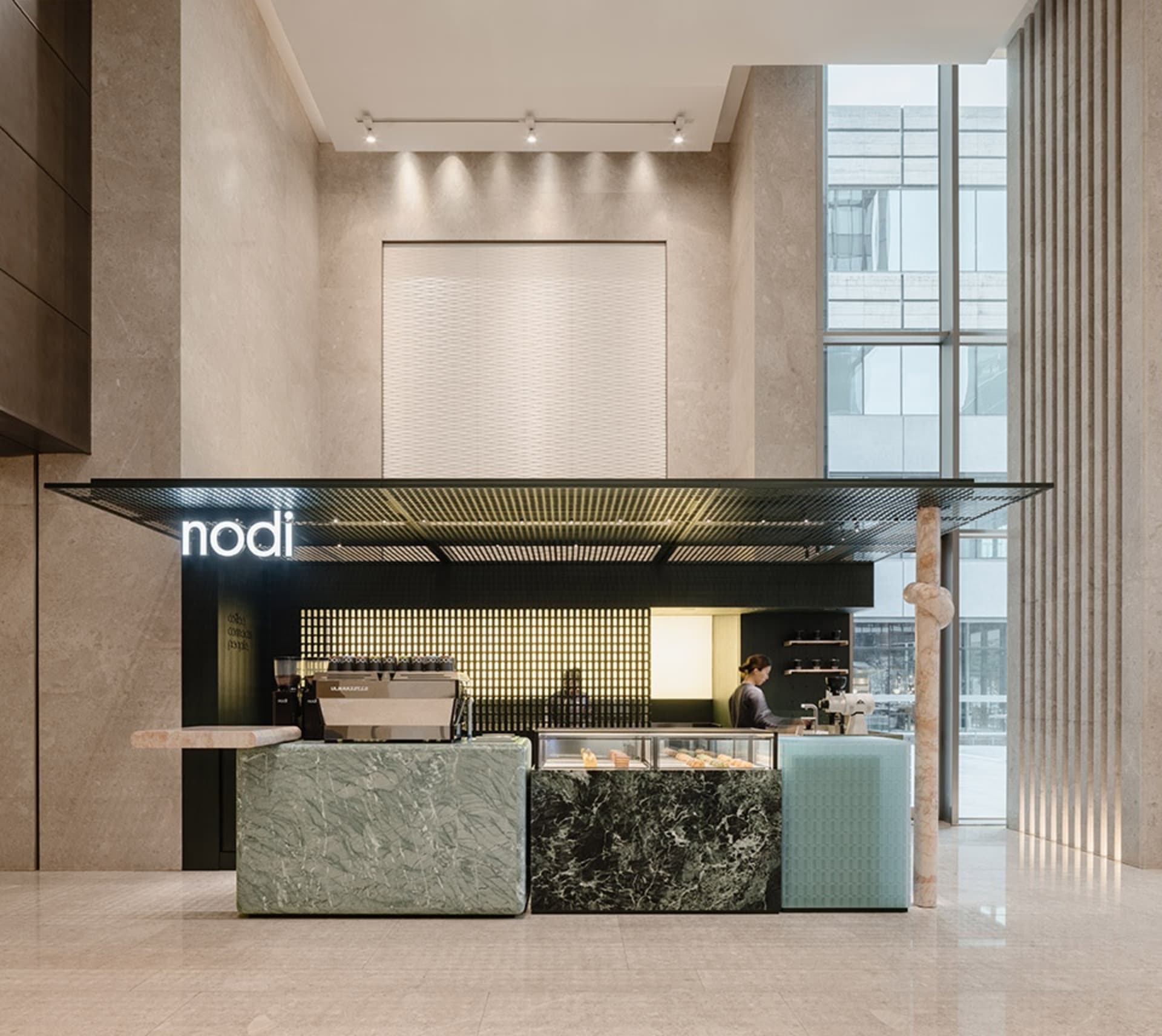 A modern cafe with a counter, couches, and a dining table, featuring marble and wood elements, natural light, and a warm atmosphere