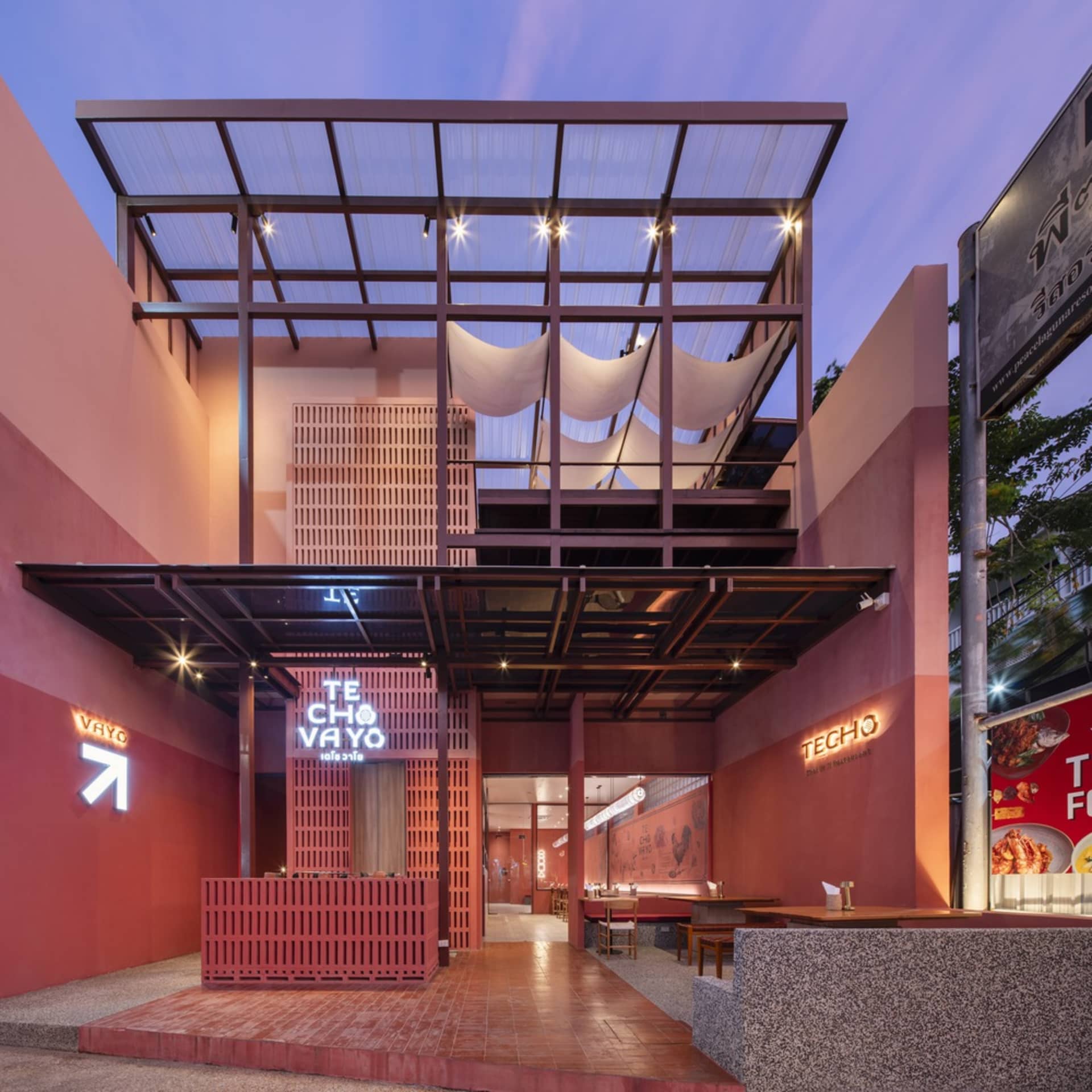 An inviting outdoor restaurant with red brick walls, dining tables, and chairs, well-lit by natural light and overhead lighting