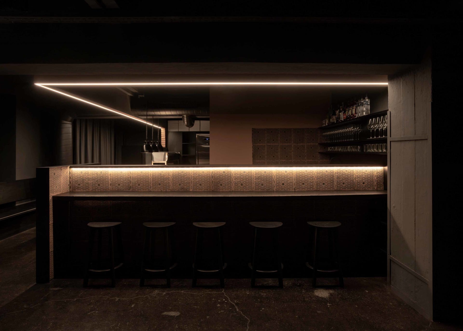 A modern bar area with a black countertop, brown wall, and four stools, creating an inviting and comfortable atmosphere