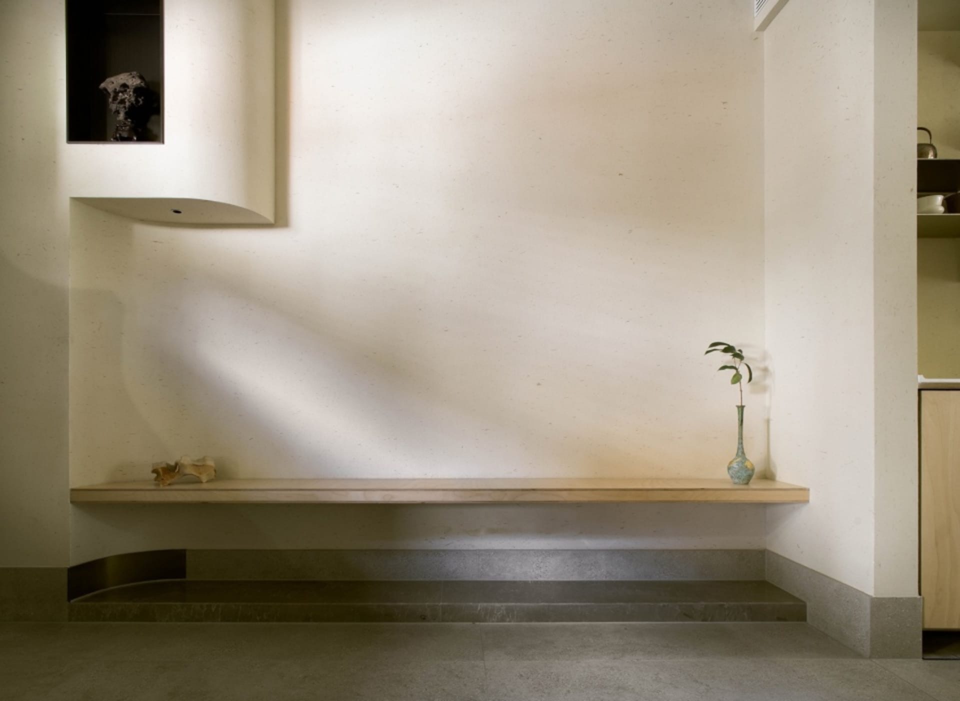 Empty room with a bench and two vases, featuring white walls and a minimalist design