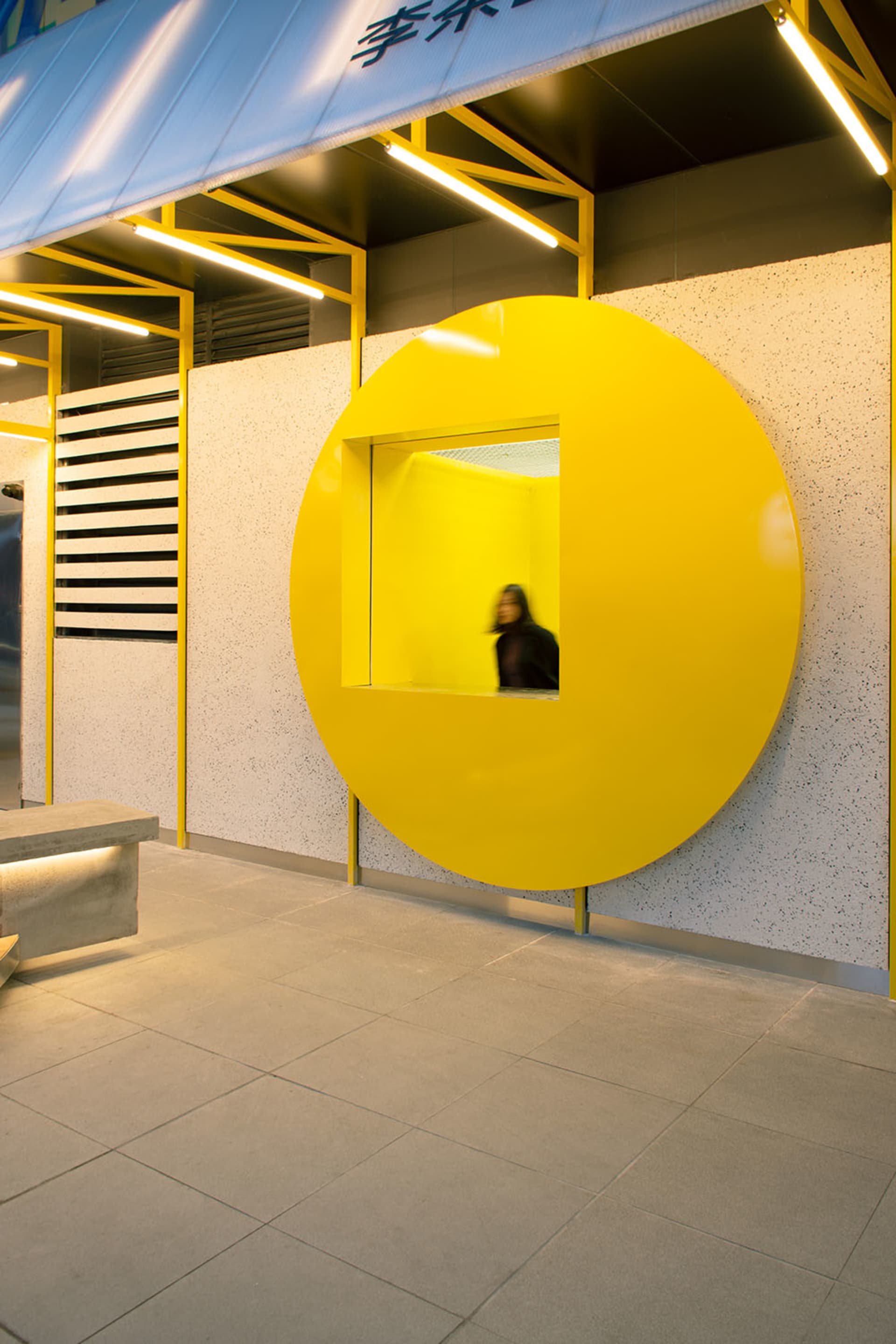 Interior space with a yellow circular window, a bench, and two people, featuring a warm and inviting atmosphere