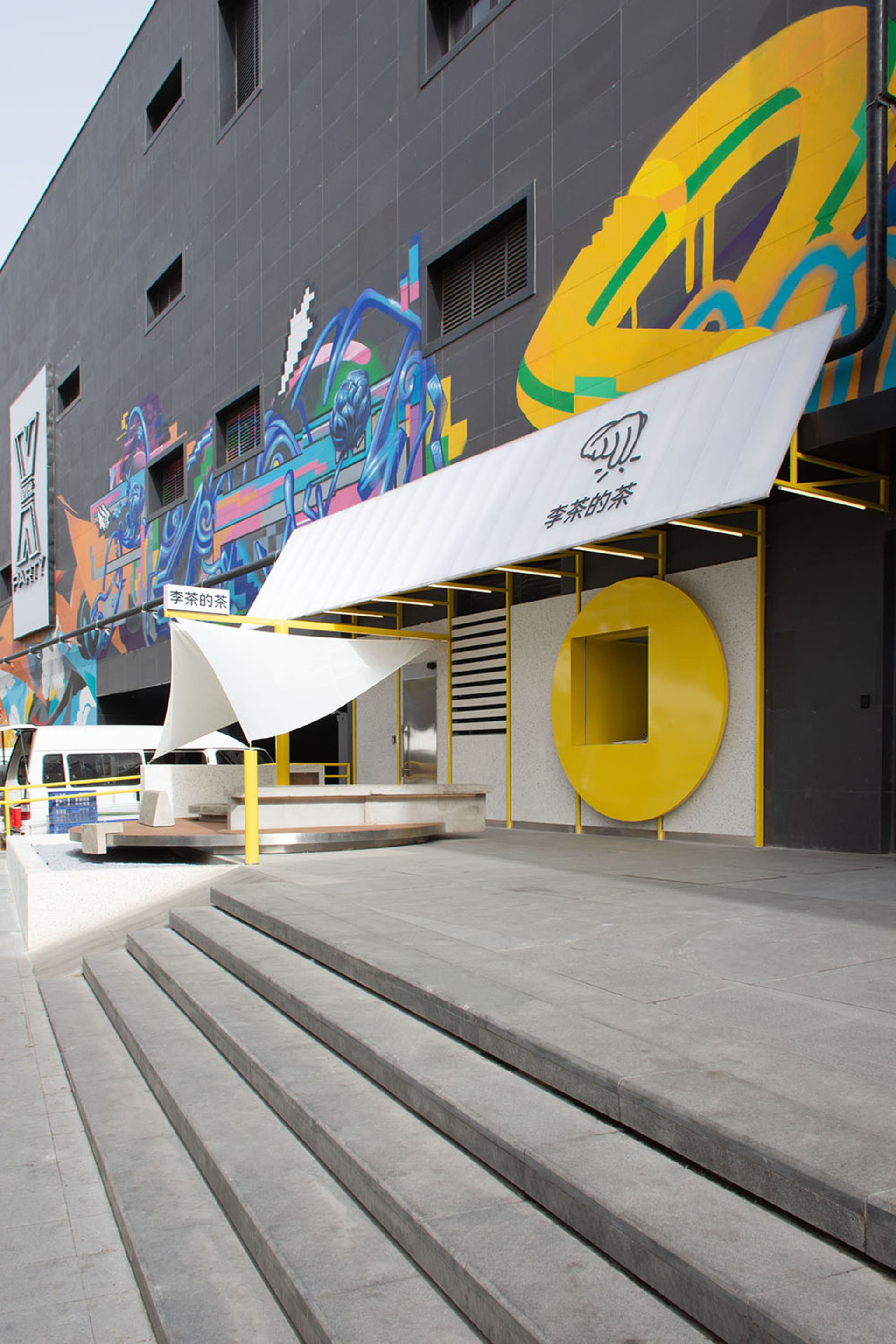 A colorful building with a yellow awning and a large white umbrella, set against a futuristic cityscape backdrop with two cars parked in front