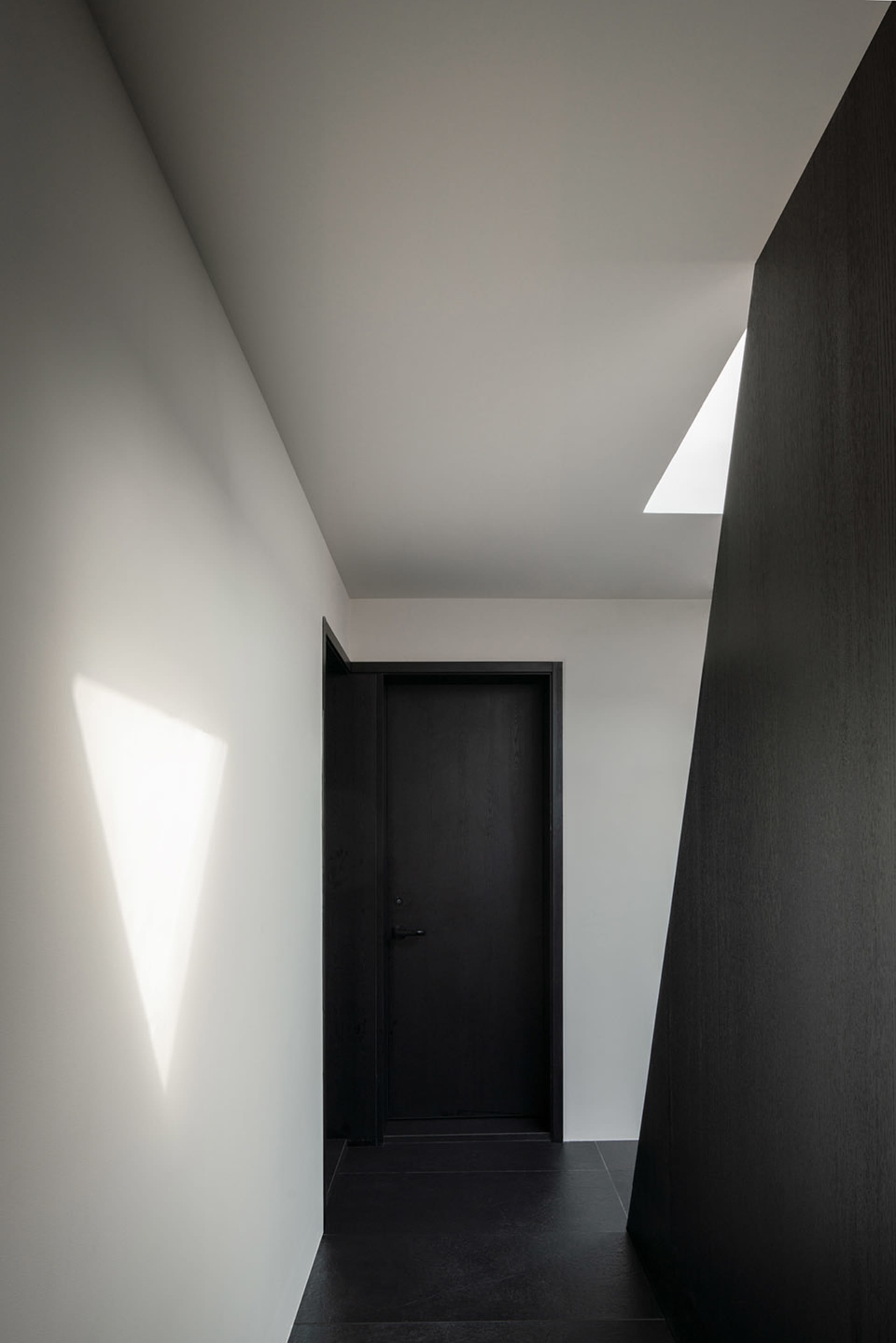 A simple hallway with a black door and a white wall, creating a striking contrast