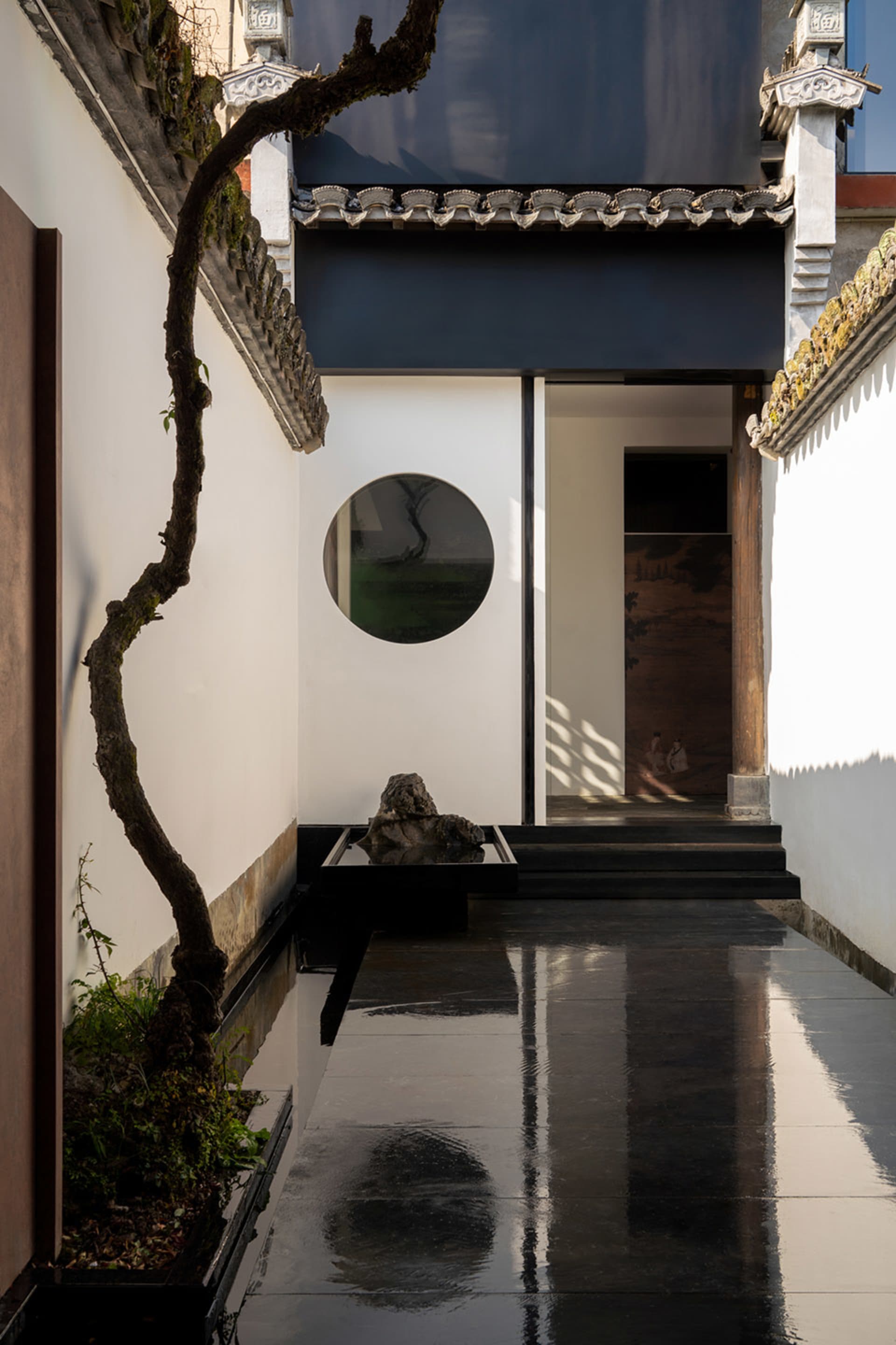 Asian-style house with a black doorway leading to a white interior featuring a circular window and a rock garden, with a modern concrete exterior and warm lighting