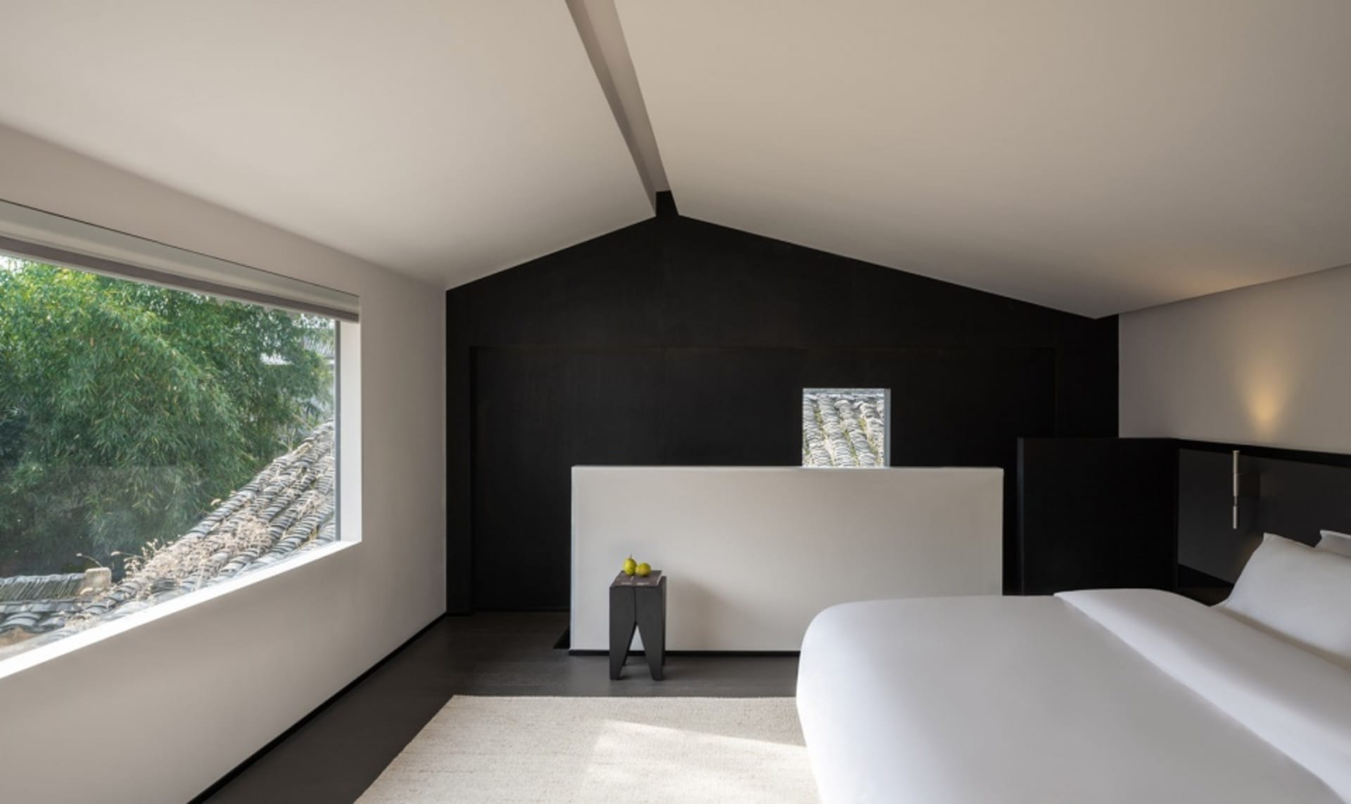 A modern bedroom with two beds, a chair, and a large window allowing natural light to enter the space