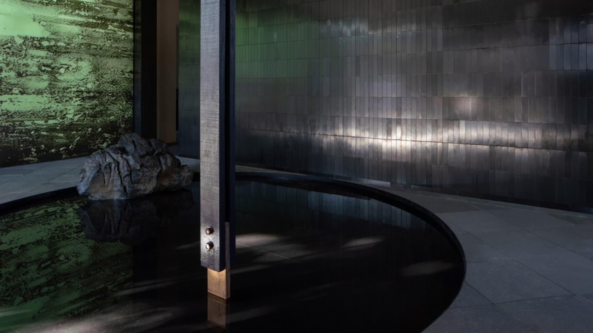 A dark and moody pool area with a black tile floor, two pools, and a prominent stone column