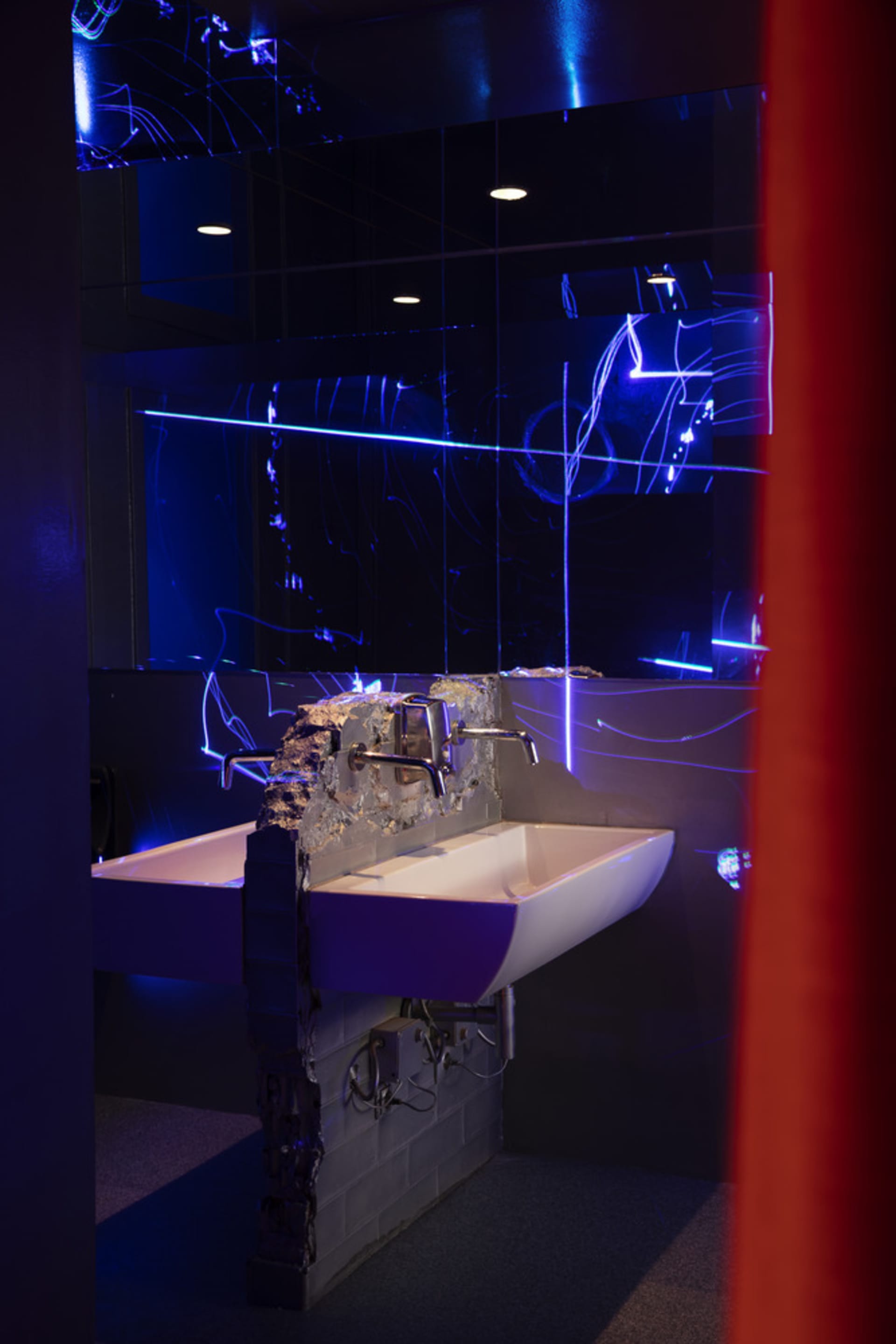 Bathroom with a metal sink, a mirror with an unusual design, and a red curtain adding a pop of color