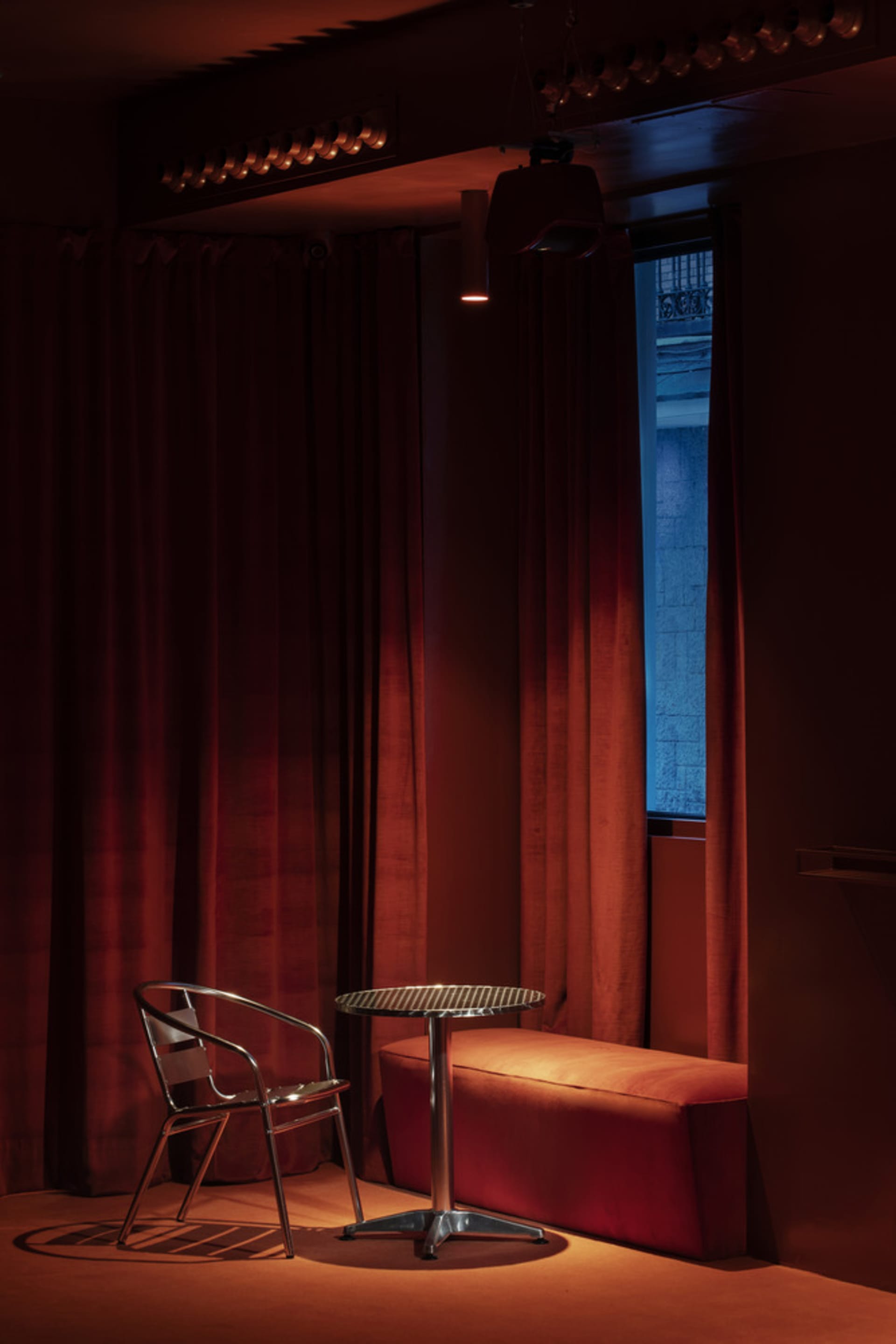 A warm and inviting room with a red curtain, a chair, a bench, and two dining tables, featuring a cozy atmosphere and elegant touches