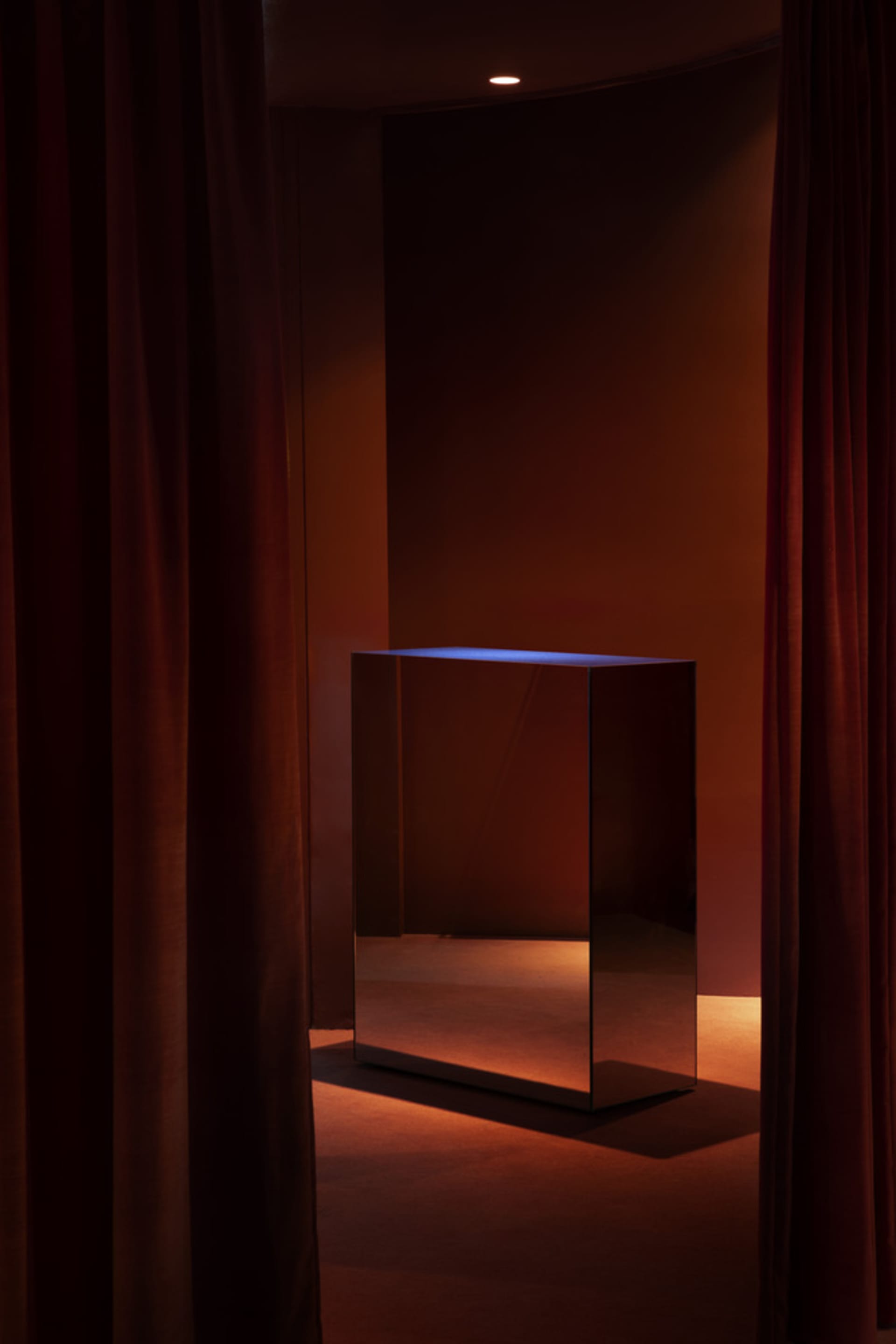 A room with a dark wood table and a large mirror in front of a curtain, creating a sophisticated atmosphere