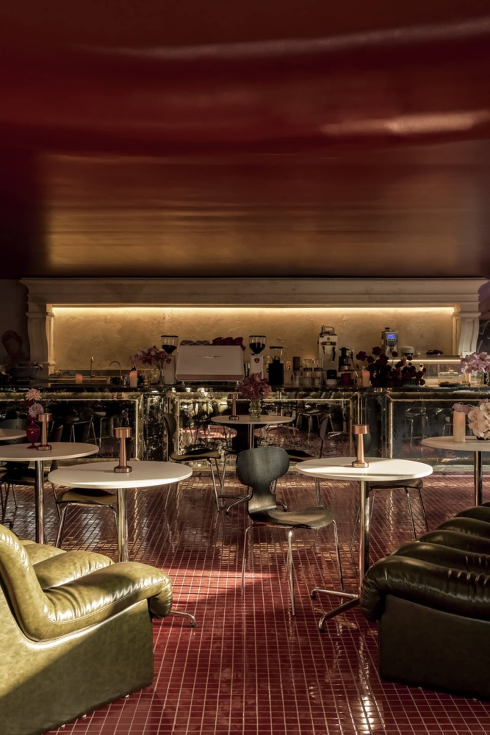 A warm and inviting restaurant interior with red walls, dining tables, chairs, and potted plants