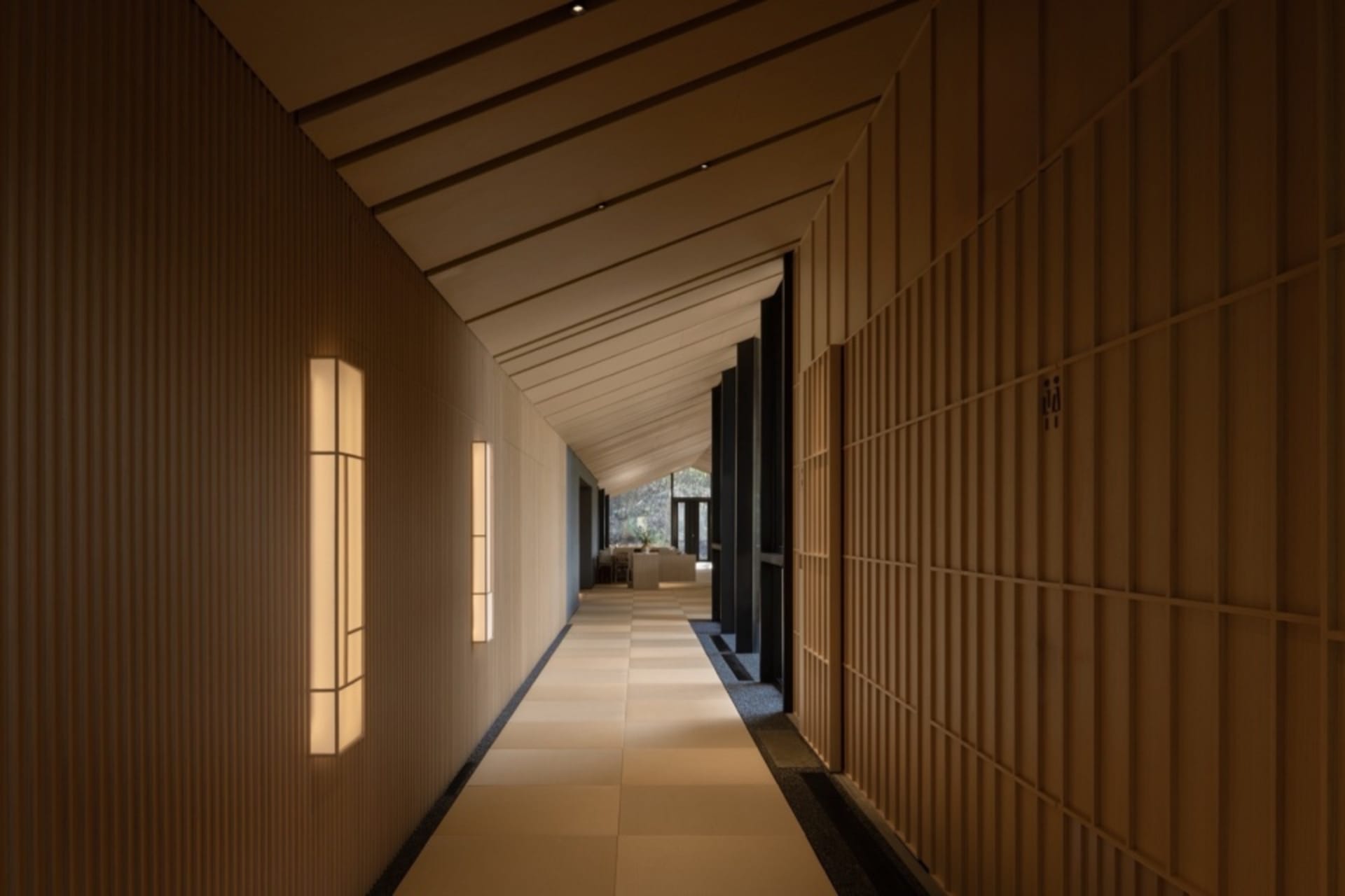 Empty hallway with wooden walls and flooring, lit by two lights on either side