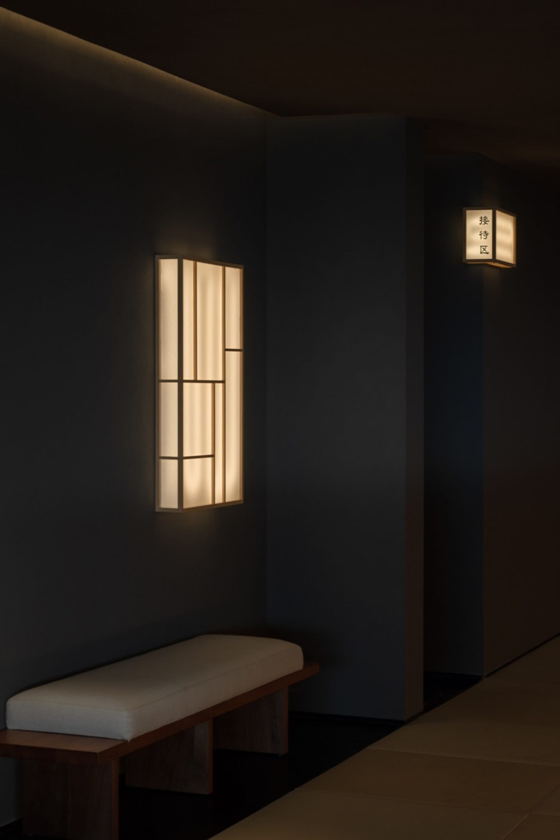 A calm and inviting hallway in an Asian home with traditional design elements, featuring two wall lights with Chinese characters and a bench against the wall