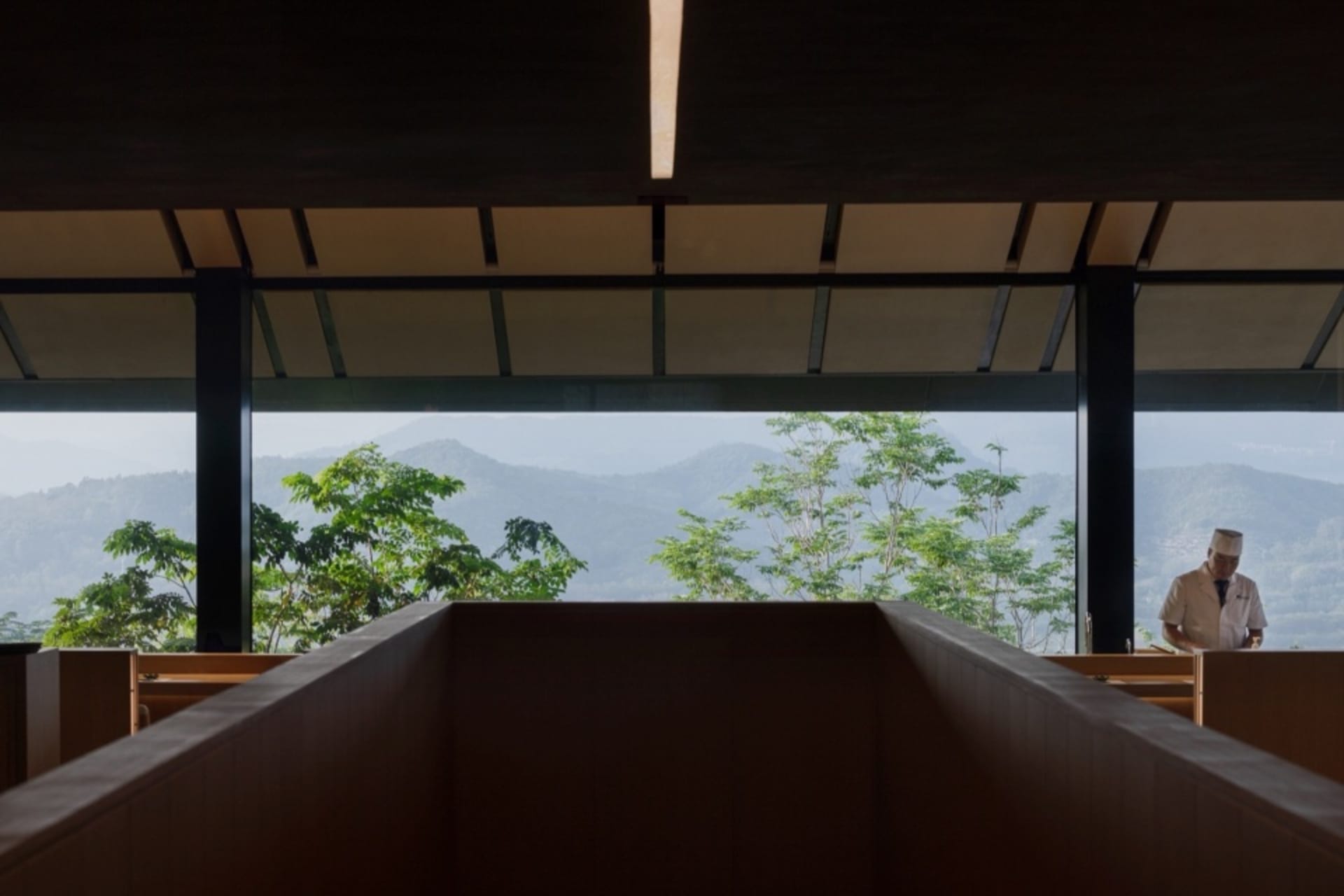 A house with a wooden facade and a large window overlooking a mountain range, creating a serene atmosphere