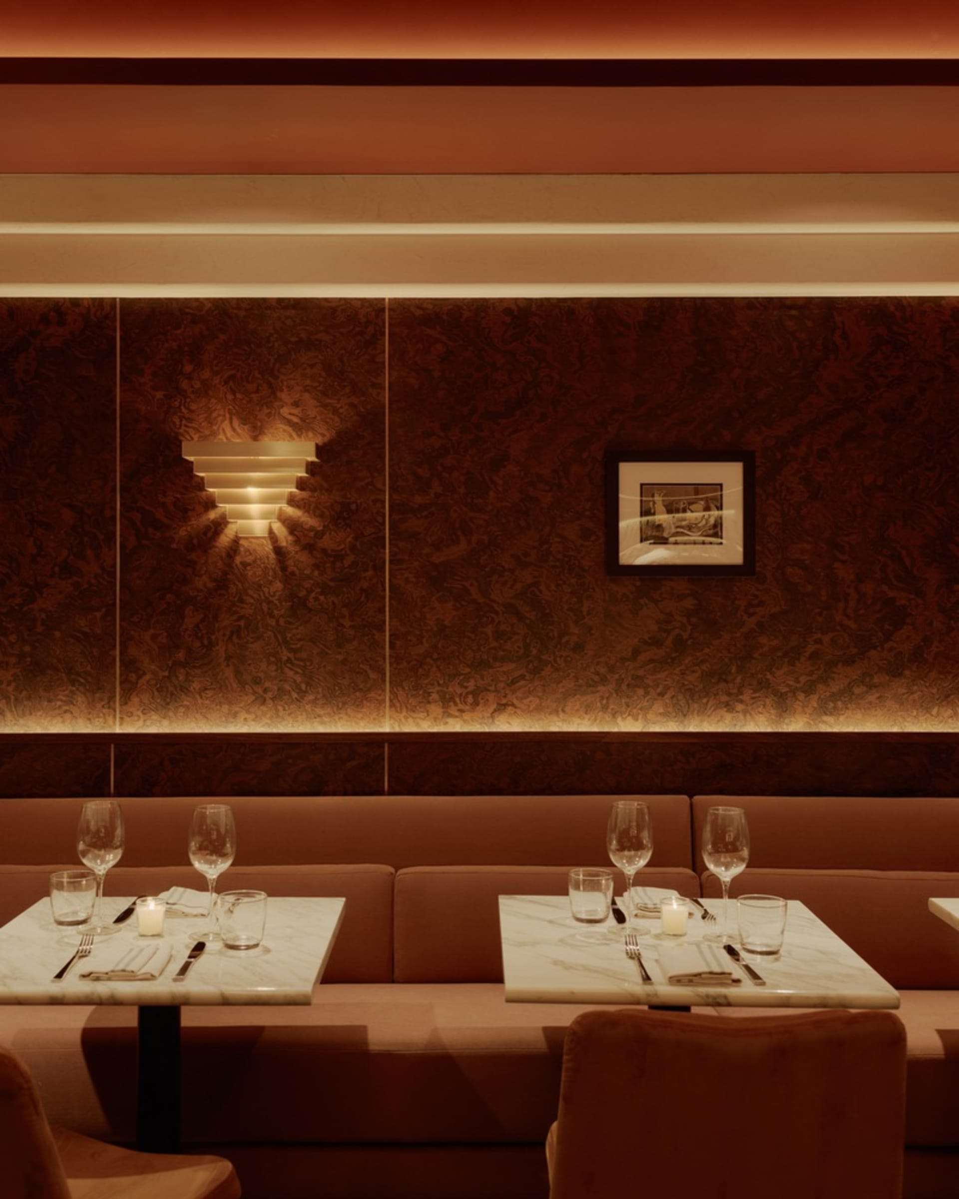 Warm and inviting restaurant interior with pink walls, brown tables, and wine glasses, candles, and chairs