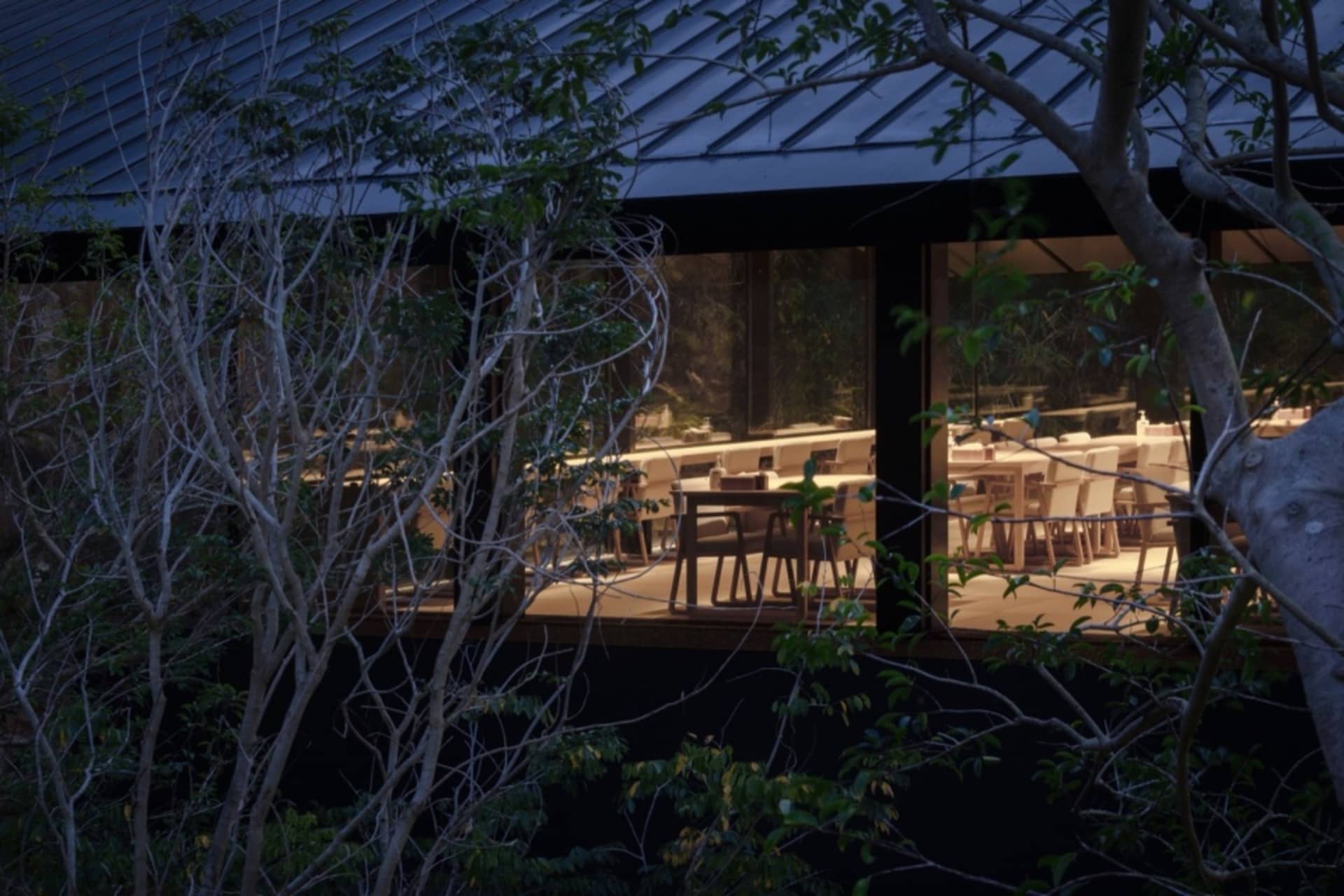 A dimly lit restaurant dining area with multiple tables and chairs, predominantly made of wood, creating a warm and inviting atmosphere