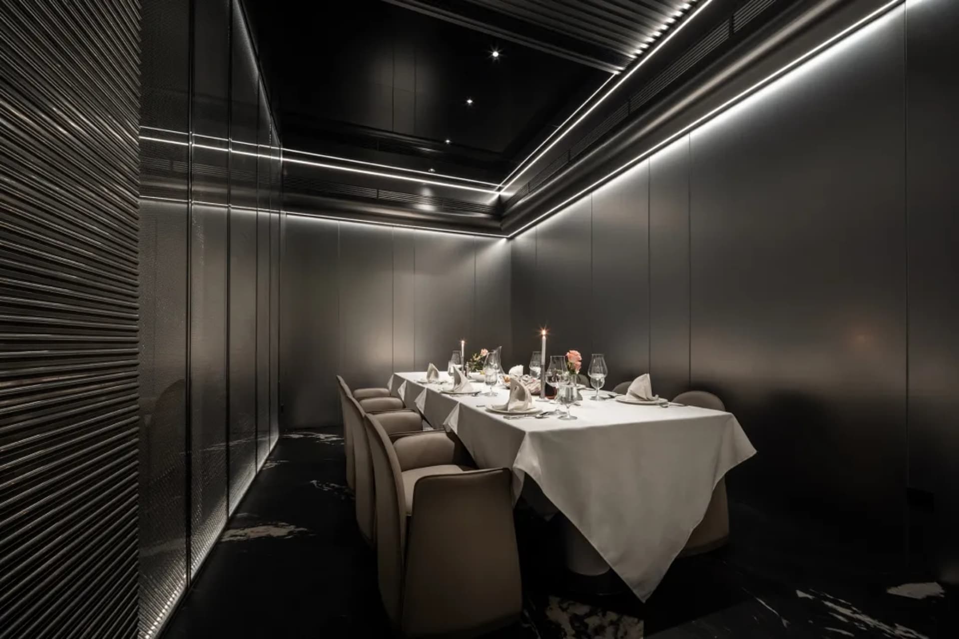 A sophisticated dining area with a long wooden table, multiple chairs, wine glasses, vases, and potted plants, perfect for special events or intimate gatherings