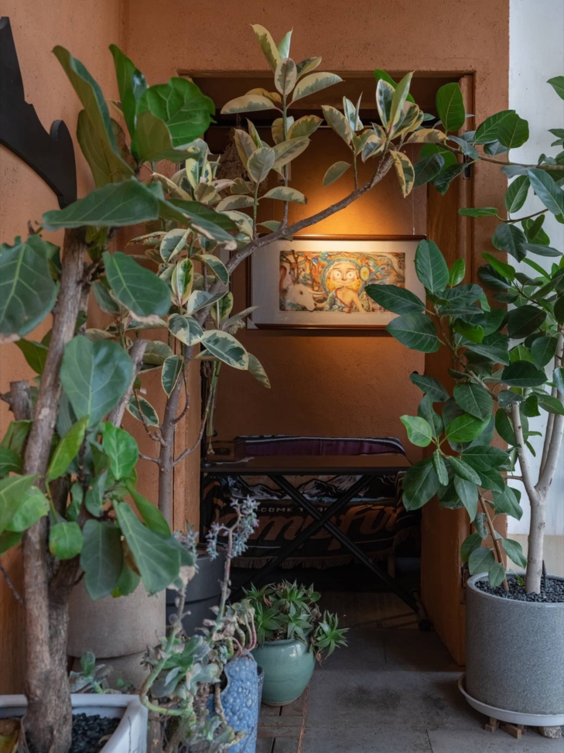 A cozy living space with potted plants, a chair, and a painting on the wall, creating a warm and inviting atmosphere