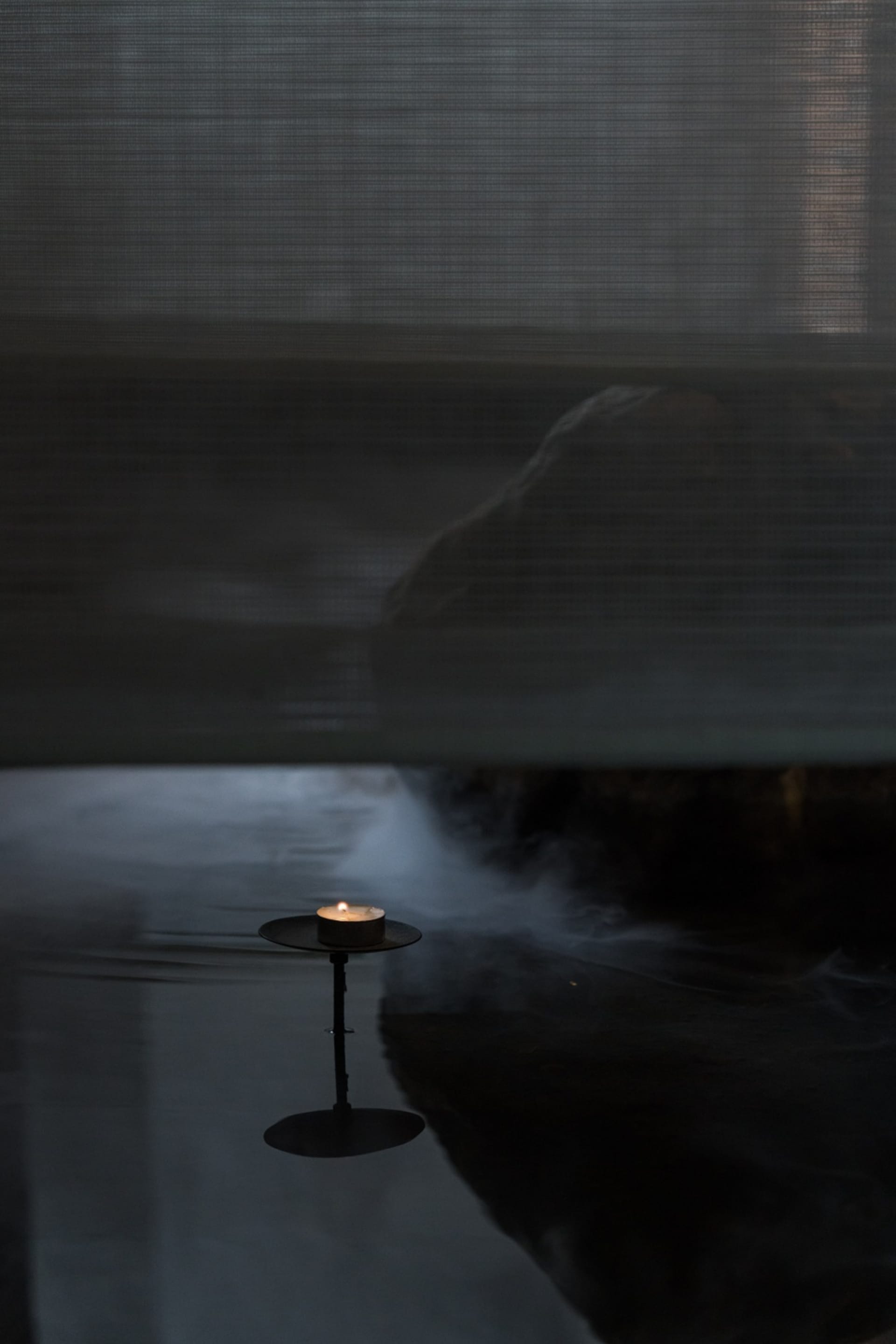 A cozy indoor space with a lit candle on a table in front of a silk curtain, creating a warm and intimate atmosphere