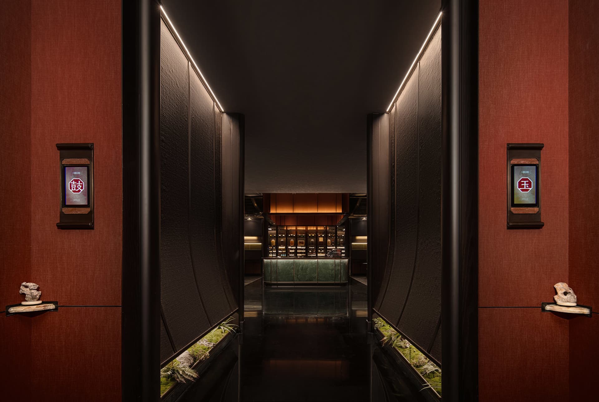 A hotel hallway with a dark carpet, potted plants, and scattered bottles, possibly leading to a bar or dining area