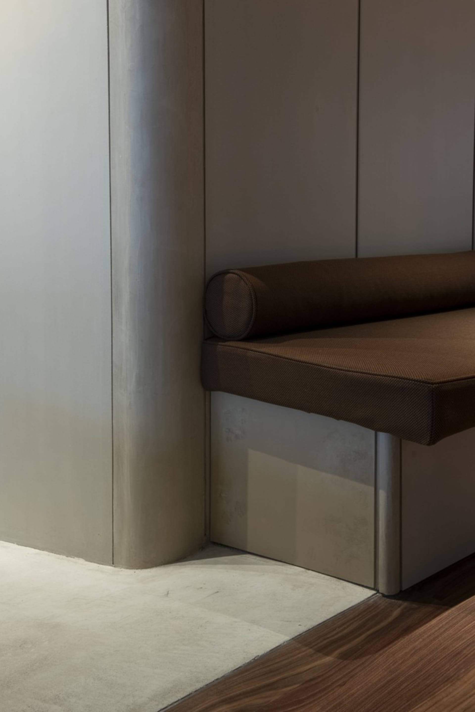 A modern and minimalist interior design featuring a wooden bench and metal accents against a silver wall, with natural light pouring in from a large window