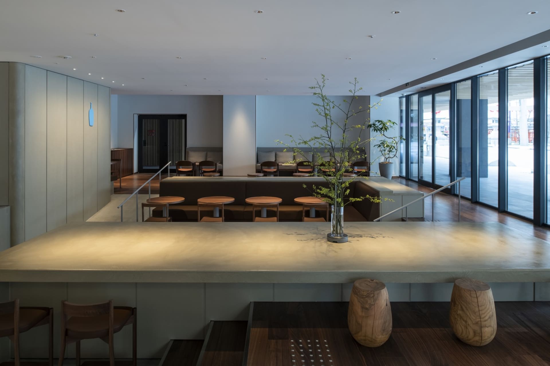 A restaurant dining area with multiple tables, chairs, and wood flooring, set against a backdrop of white and grey walls