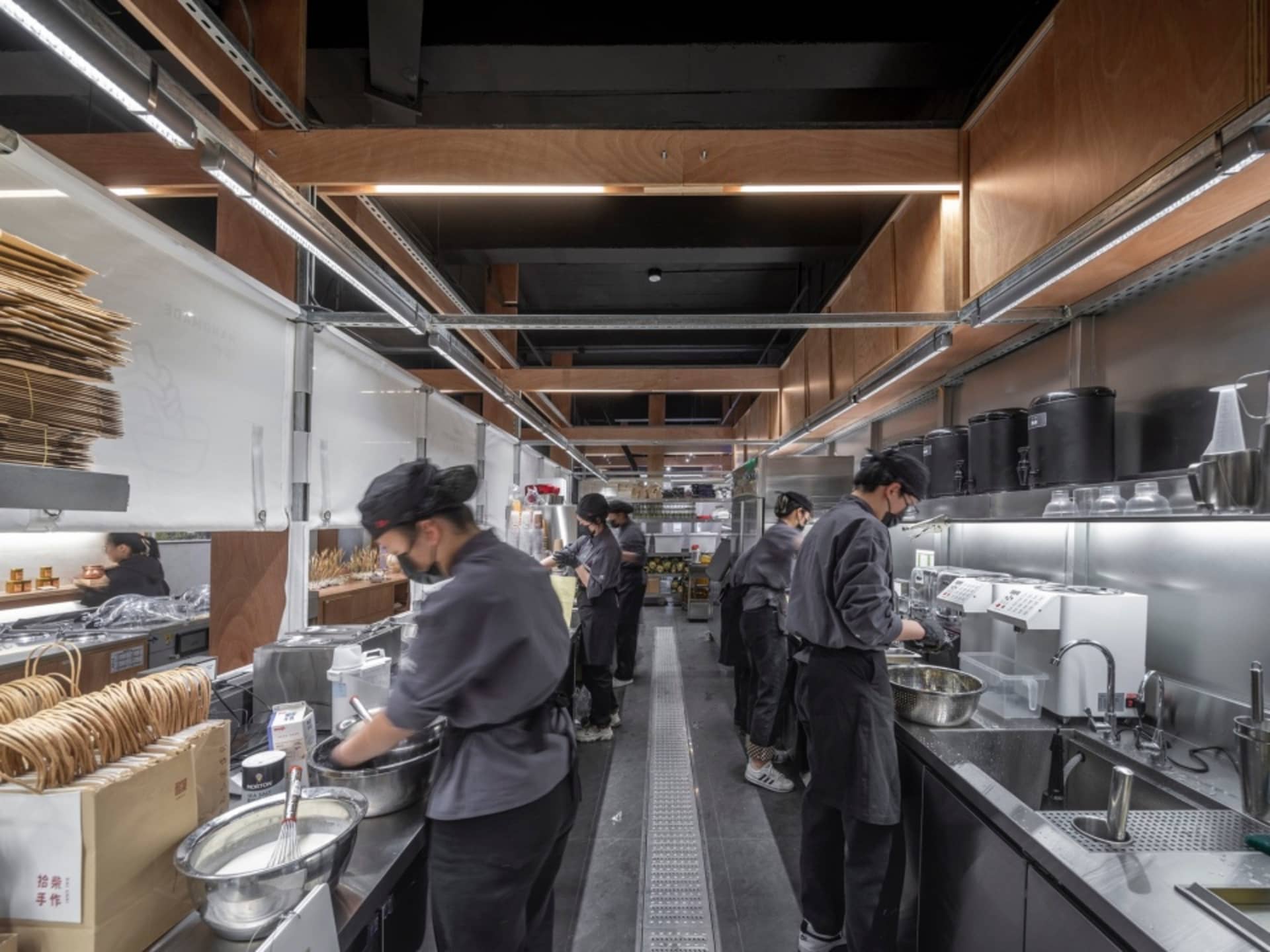 A bustling commercial kitchen with multiple people preparing food, featuring modern appliances, ovens, and scattered bottles, set against a busy and dynamic atmosphere