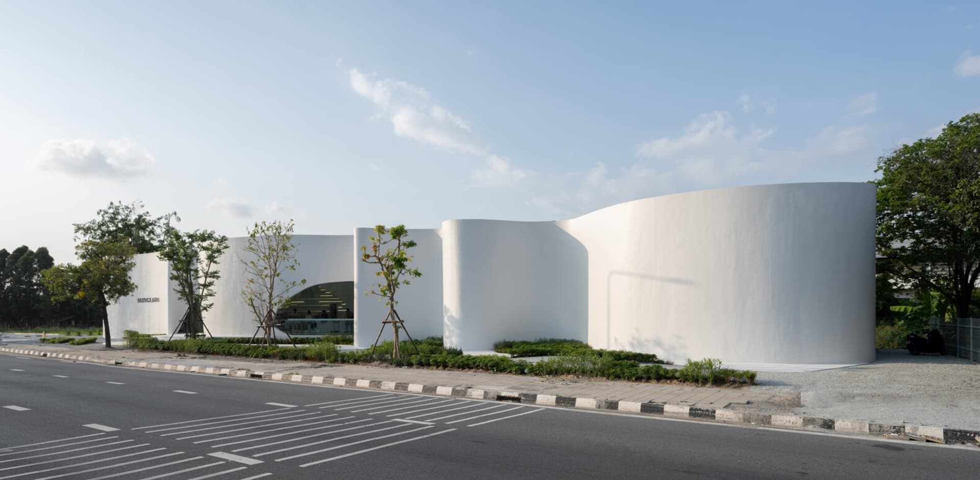 A modern building with a curved design and a circular window, surrounded by potted plants and featuring two people in the scene