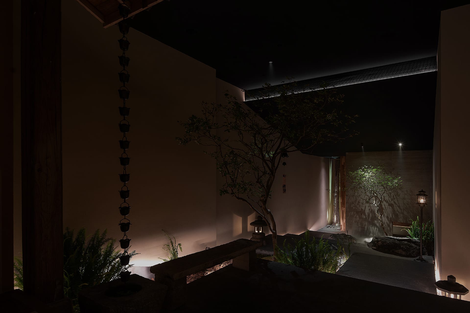 Cozy indoor space with a stone wall, a tree, and potted plants, dimly lit for a warm ambiance