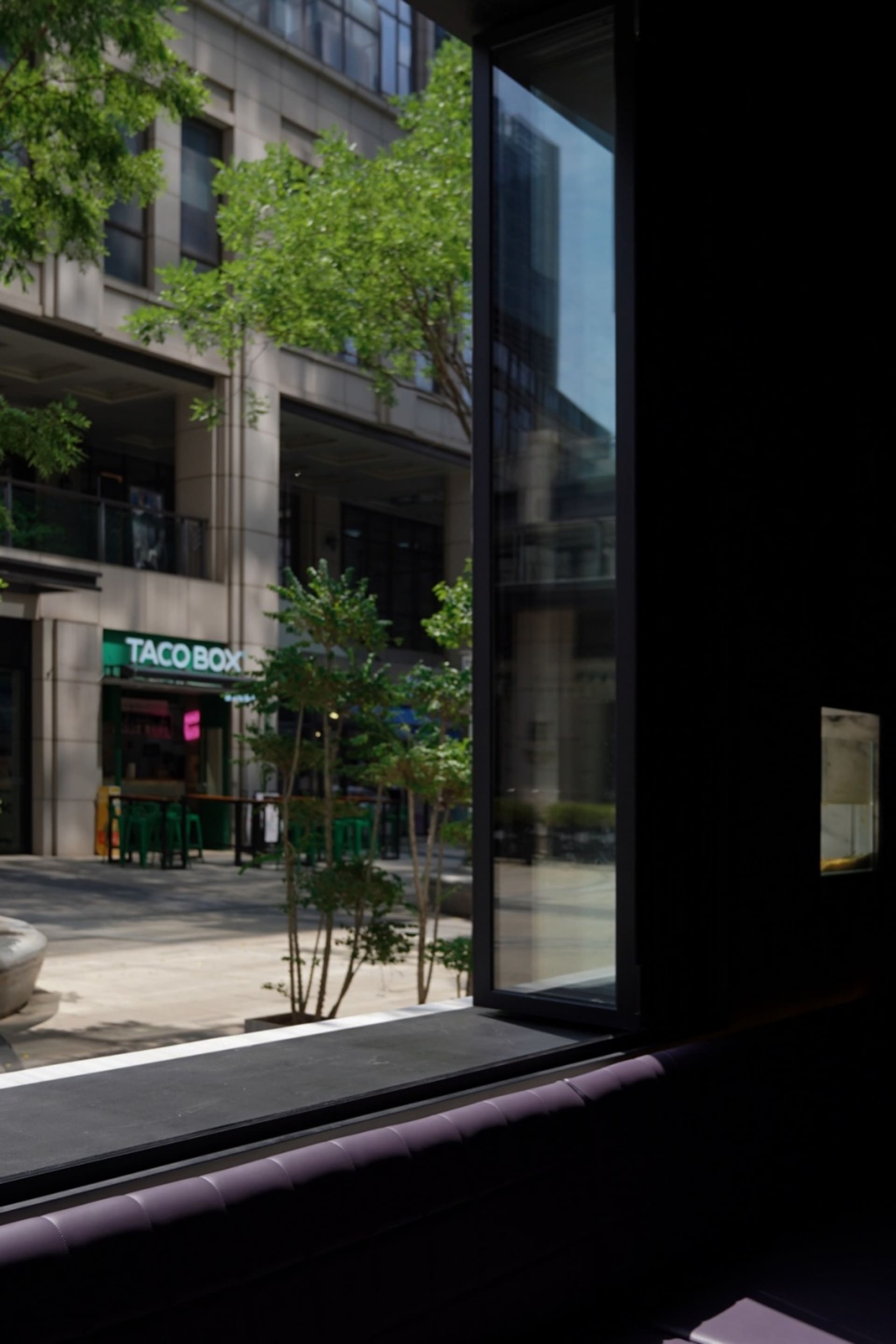 A modern building with a glass facade and outdoor seating area, set amidst a lively urban street scene