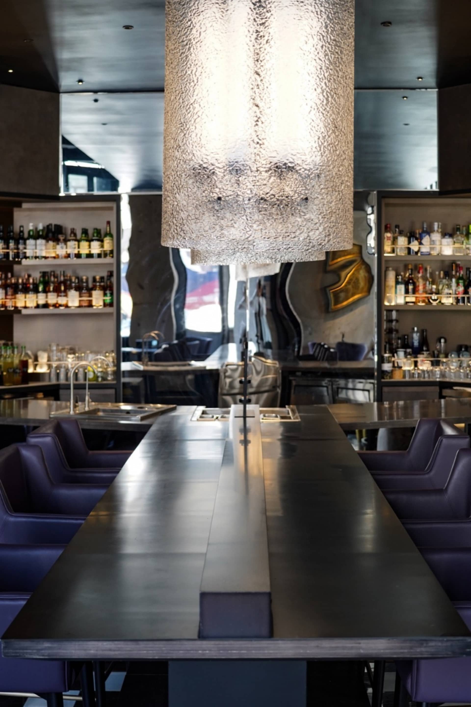 A casual bar area with a large dining table surrounded by chairs, bottles, and a comfortable atmosphere