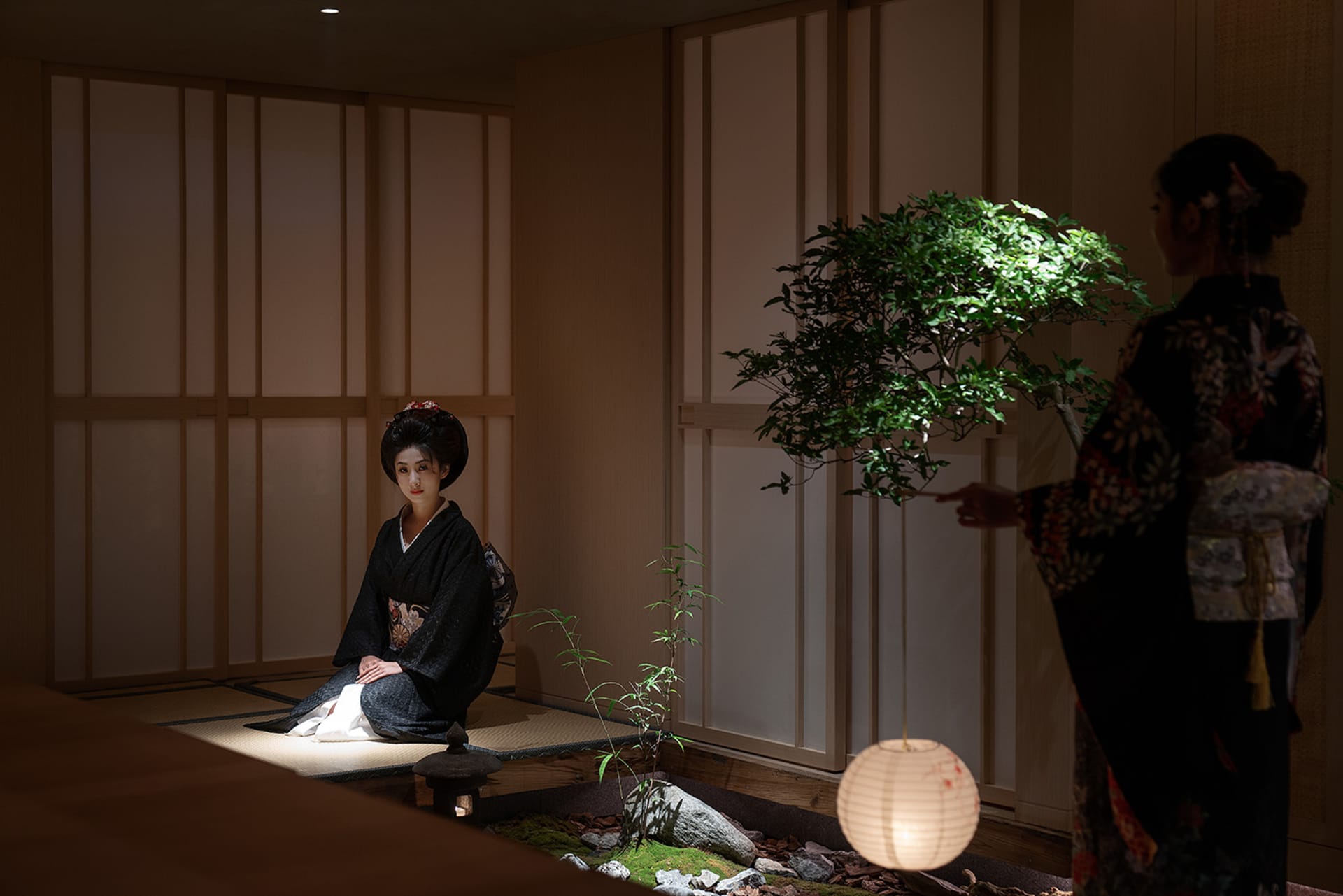 A serene and contemplative scene of an Asian woman sitting on the ground in a dimly lit room with wooden walls and floors, featuring a small potted plant