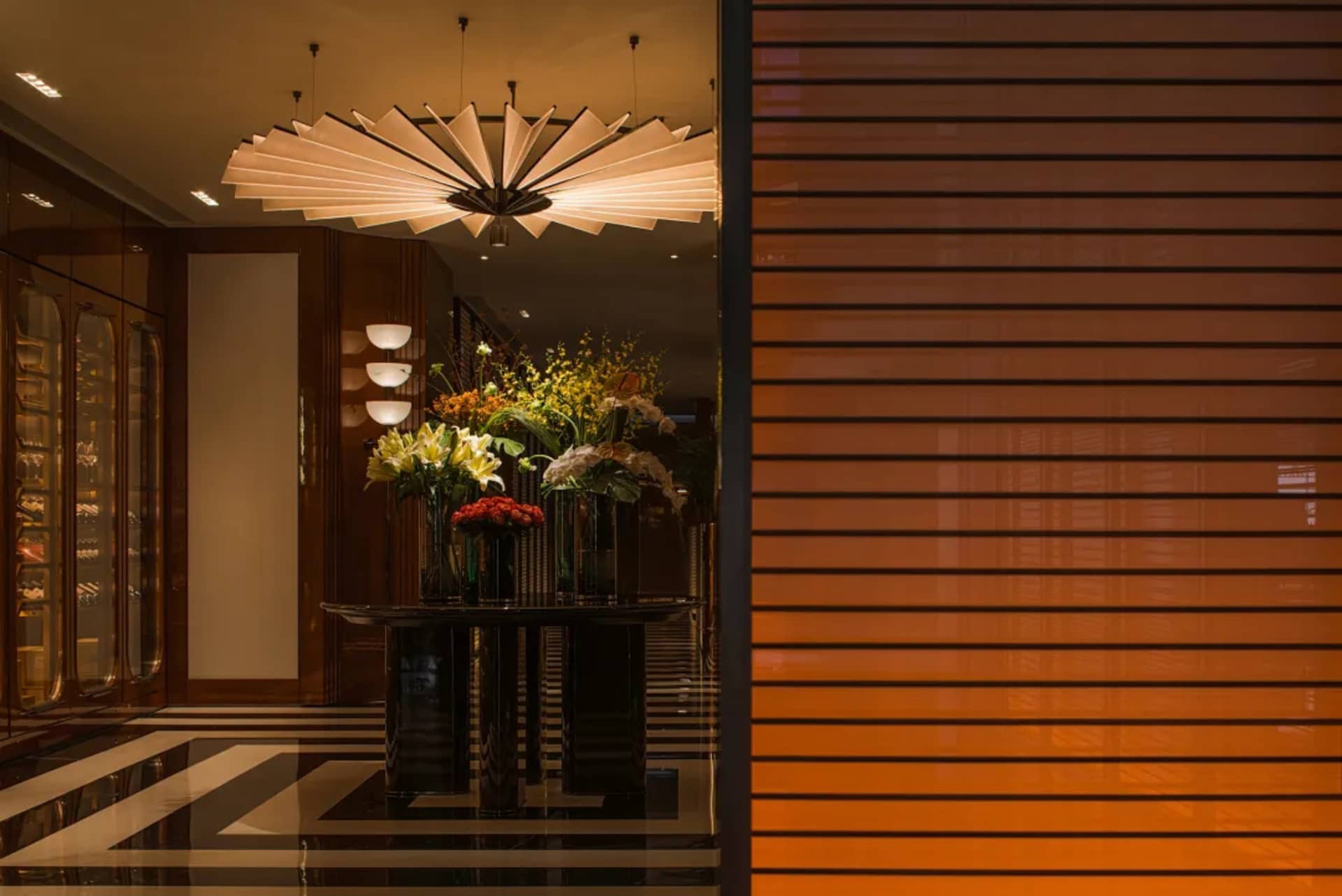 A well-lit room with a large black table, potted plants, and a vase of flowers, creating a warm and inviting atmosphere