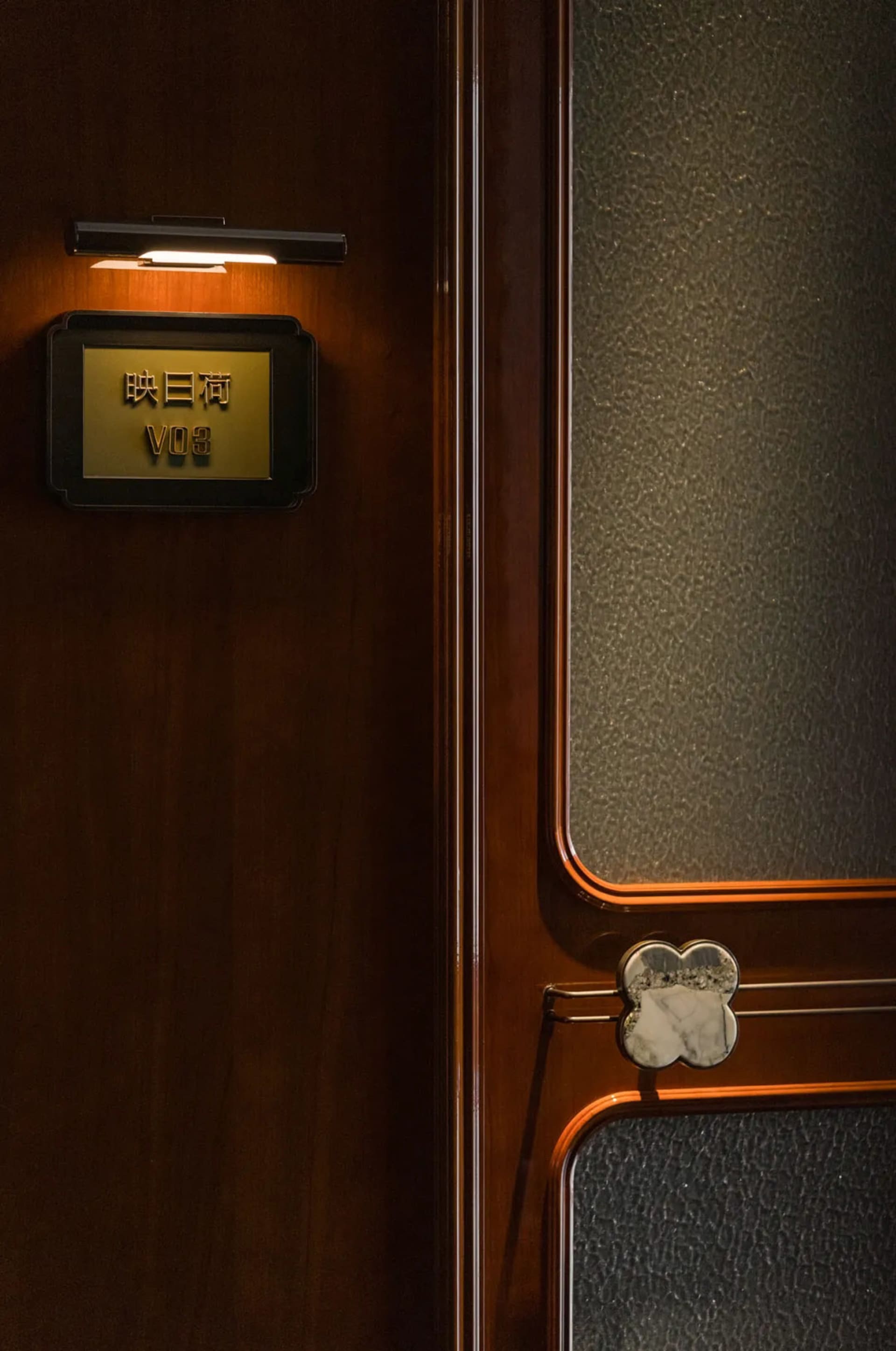 A warm and inviting Asian-style interior space with a wooden door featuring a small window and a gold sign, set against a neutral background