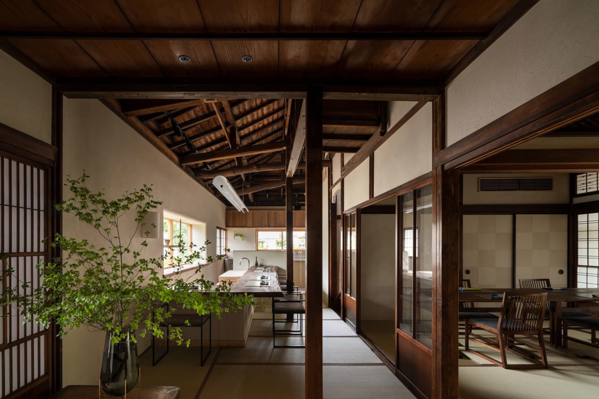 A well-lit, inviting space with wooden floors and walls, featuring a dining area, kitchen, and living room with a couch and potted plants