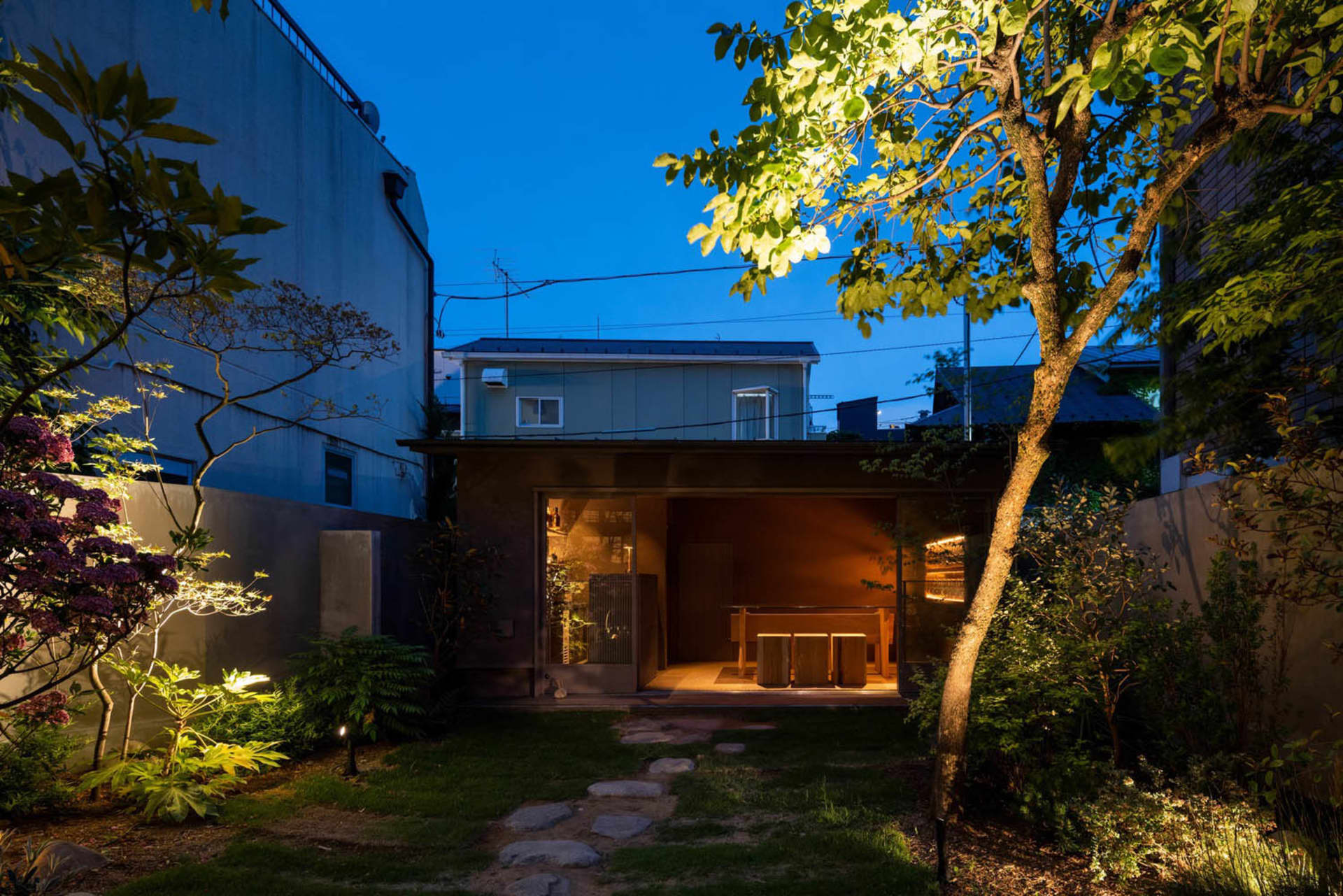 A cozy outdoor dining space with two tables and chairs on a patio, illuminated by night lights