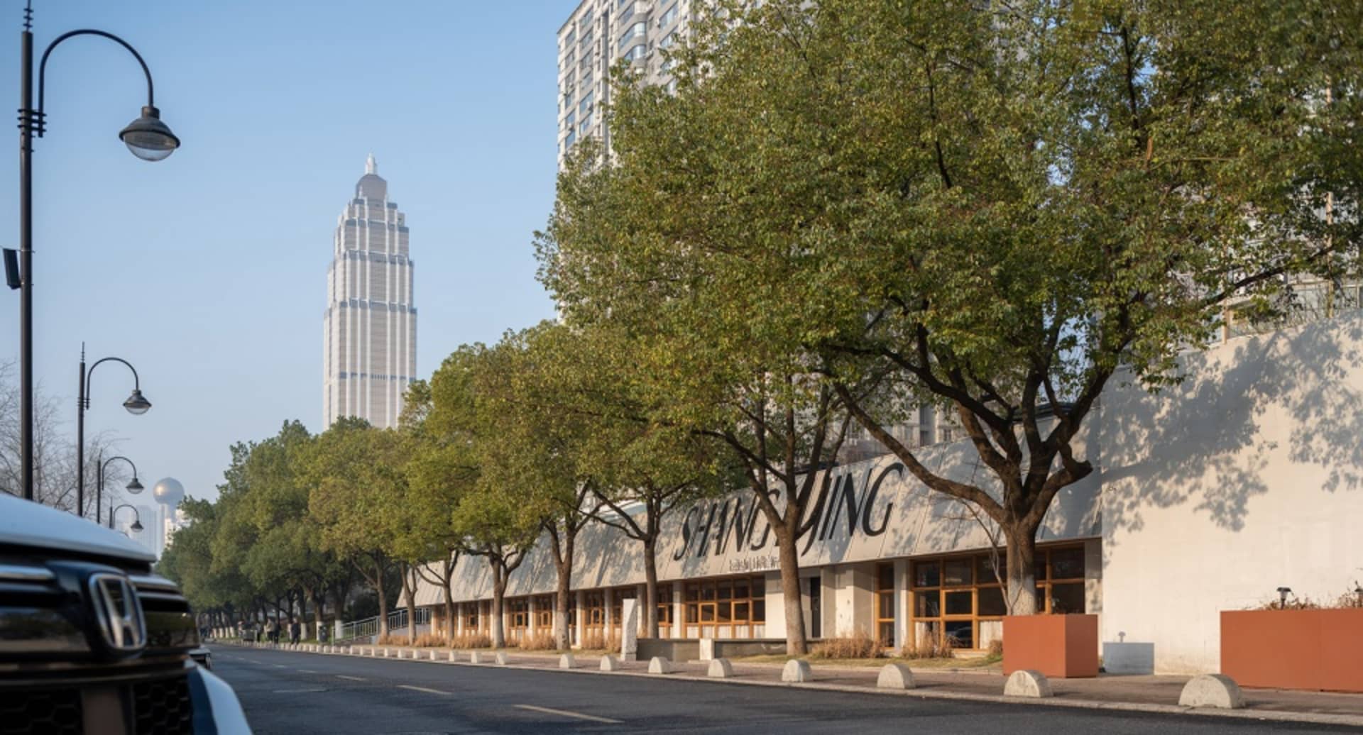 A modern building with a glass facade and white exterior, surrounded by trees and a bustling city atmosphere