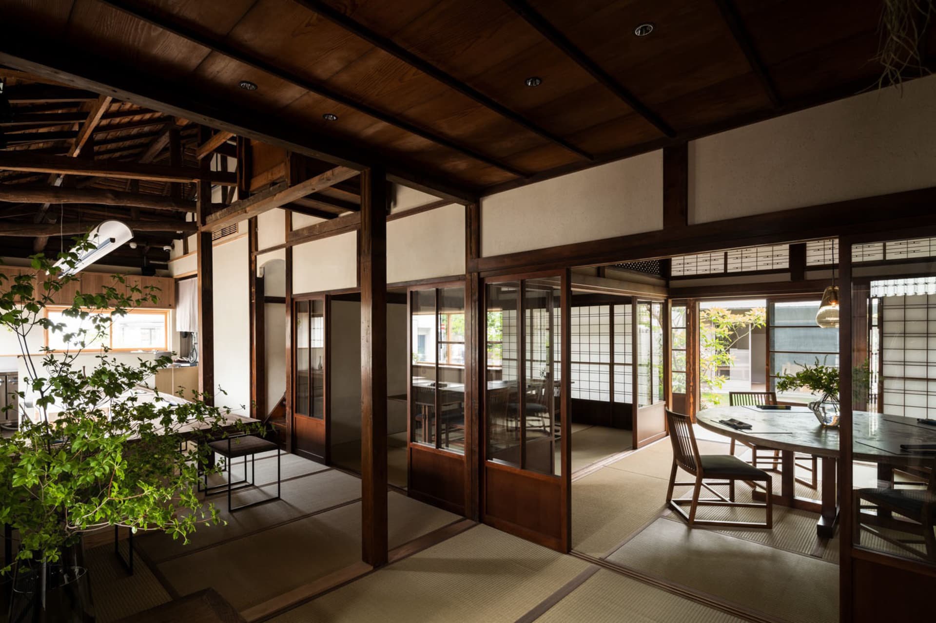 Warm and inviting living area with wooden floors and walls, featuring traditional Asian design elements, chairs, dining tables, and potted plants