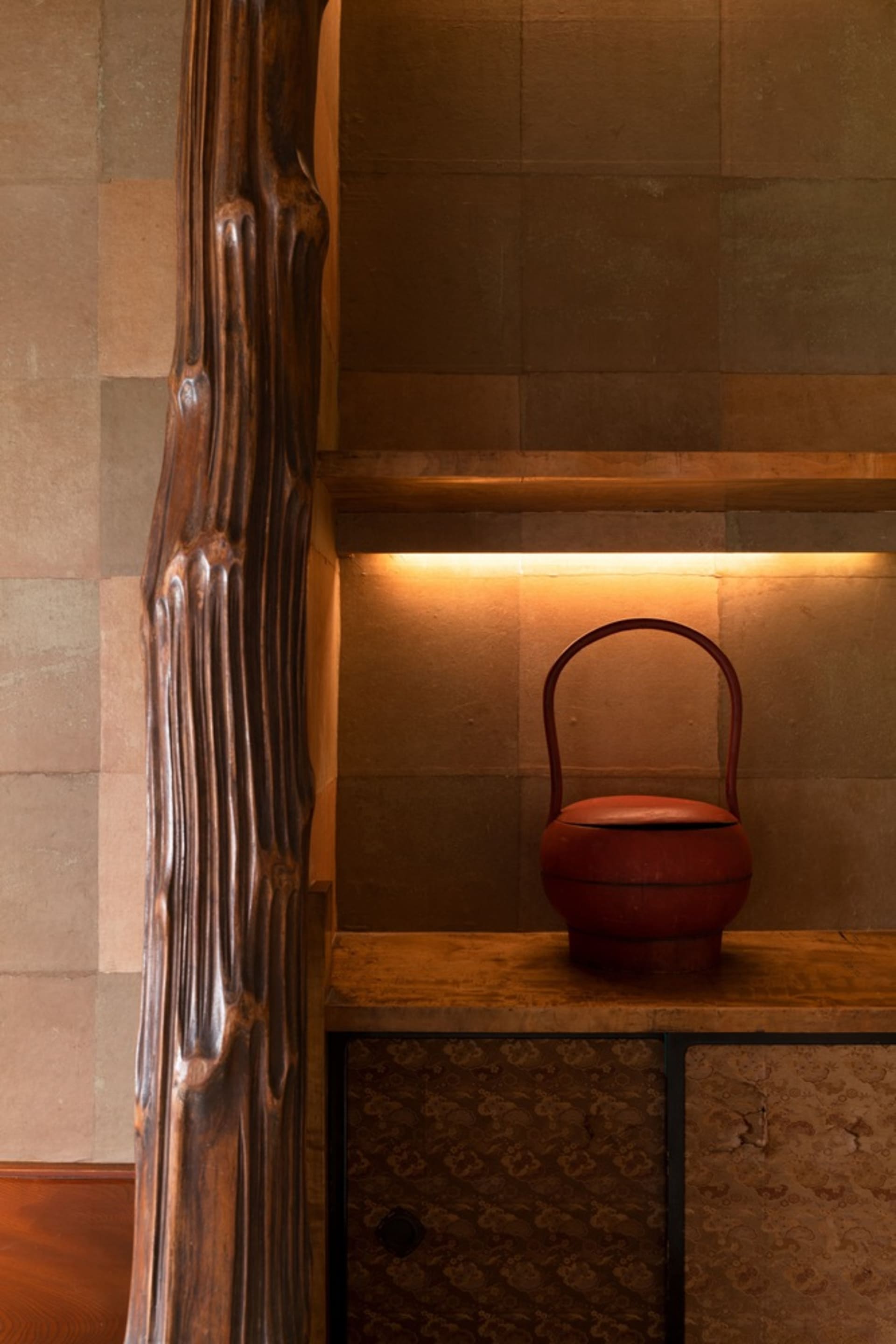 A wooden table with a red clay vase on a wall in a rustic living space