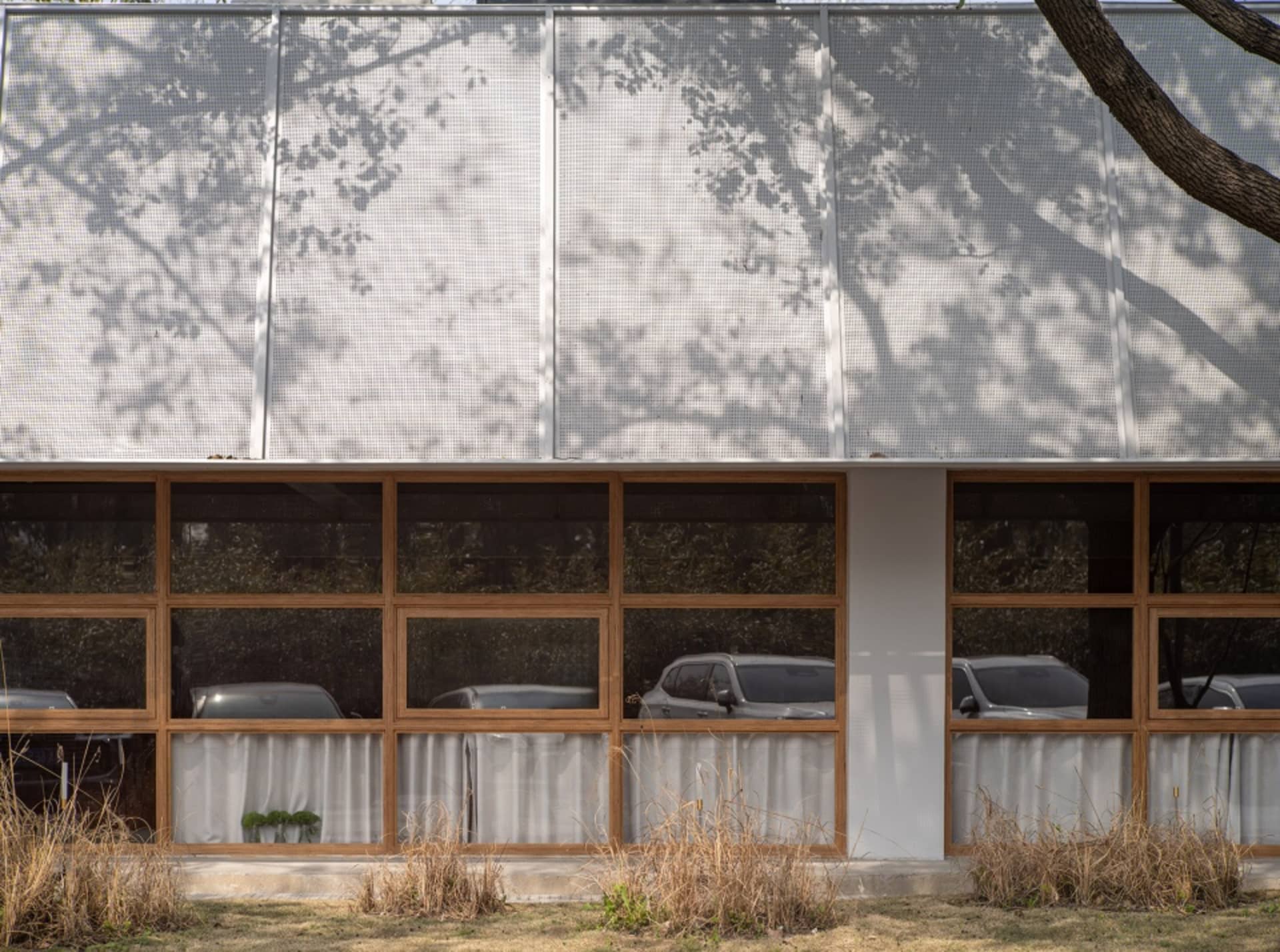 A modern building with white walls and wooden elements, featuring multiple windows and a clean design, with two cars parked in front