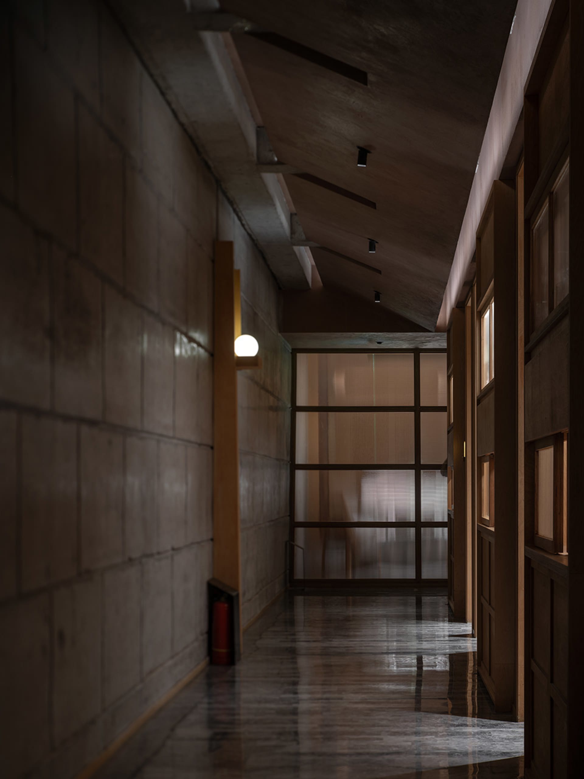 Empty hotel hallway with a concrete floor, glass doors, and two chairs for seating