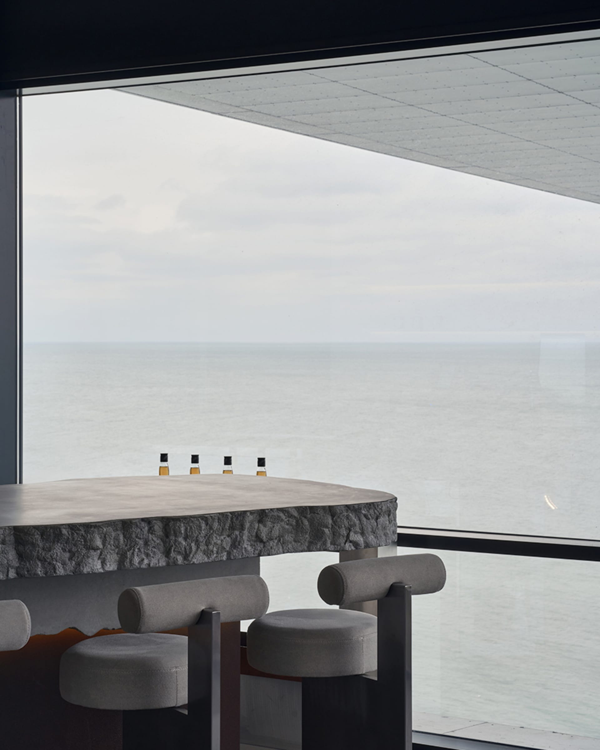 A serene coastal balcony with two chairs and a table with three bottles, offering a beautiful ocean view